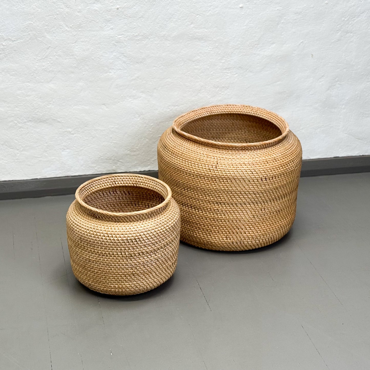 Two woven baskets on a plain floor with a light gray wall background