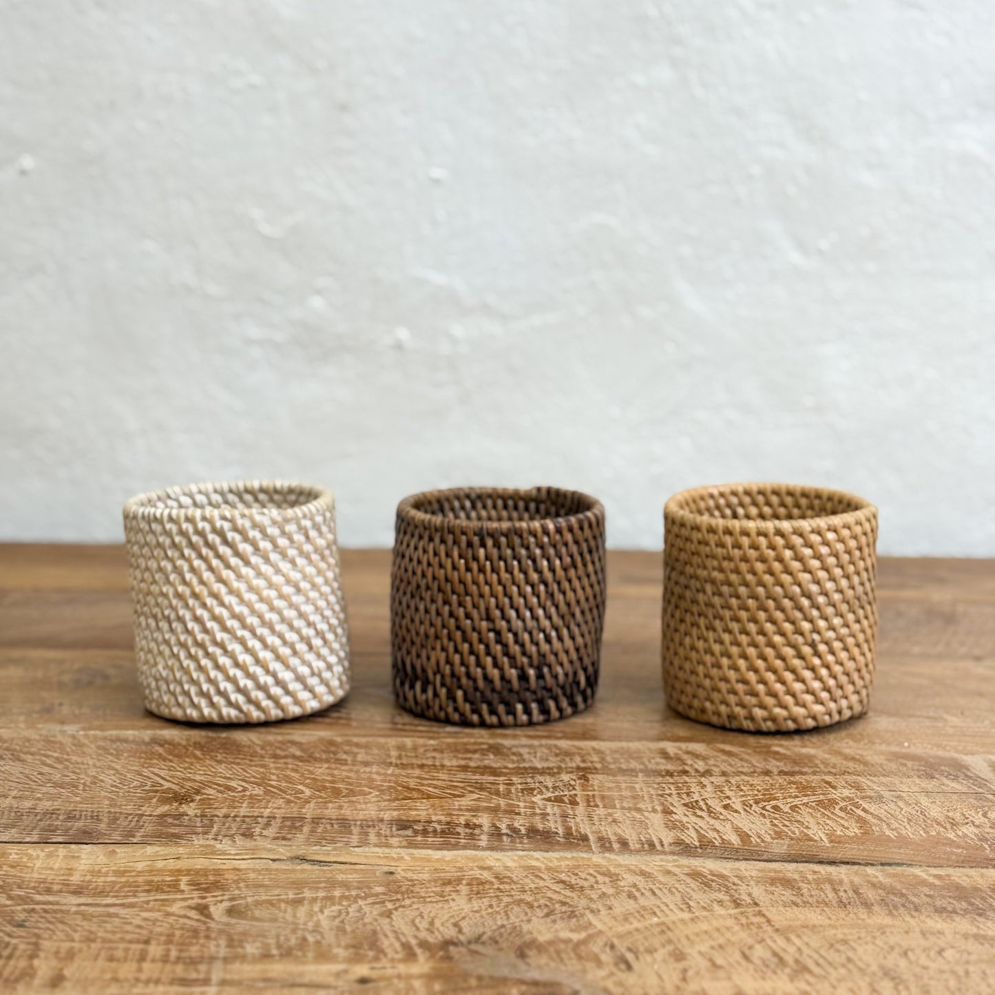Three woven baskets of different colors on a wooden surface with a light gray background