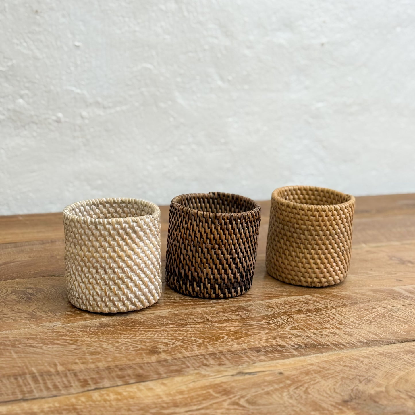 Three woven baskets of different colors on a wooden surface with a light gray background