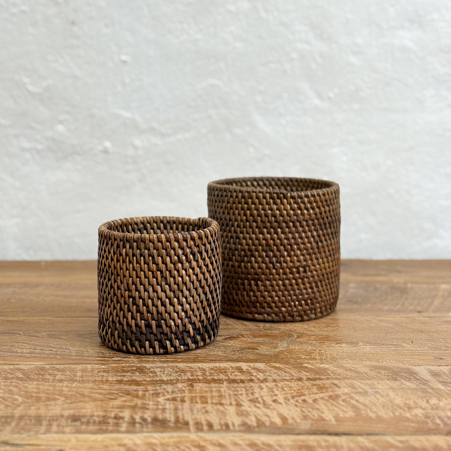 Two woven brown baskets on a wooden surface with a light gray textured background