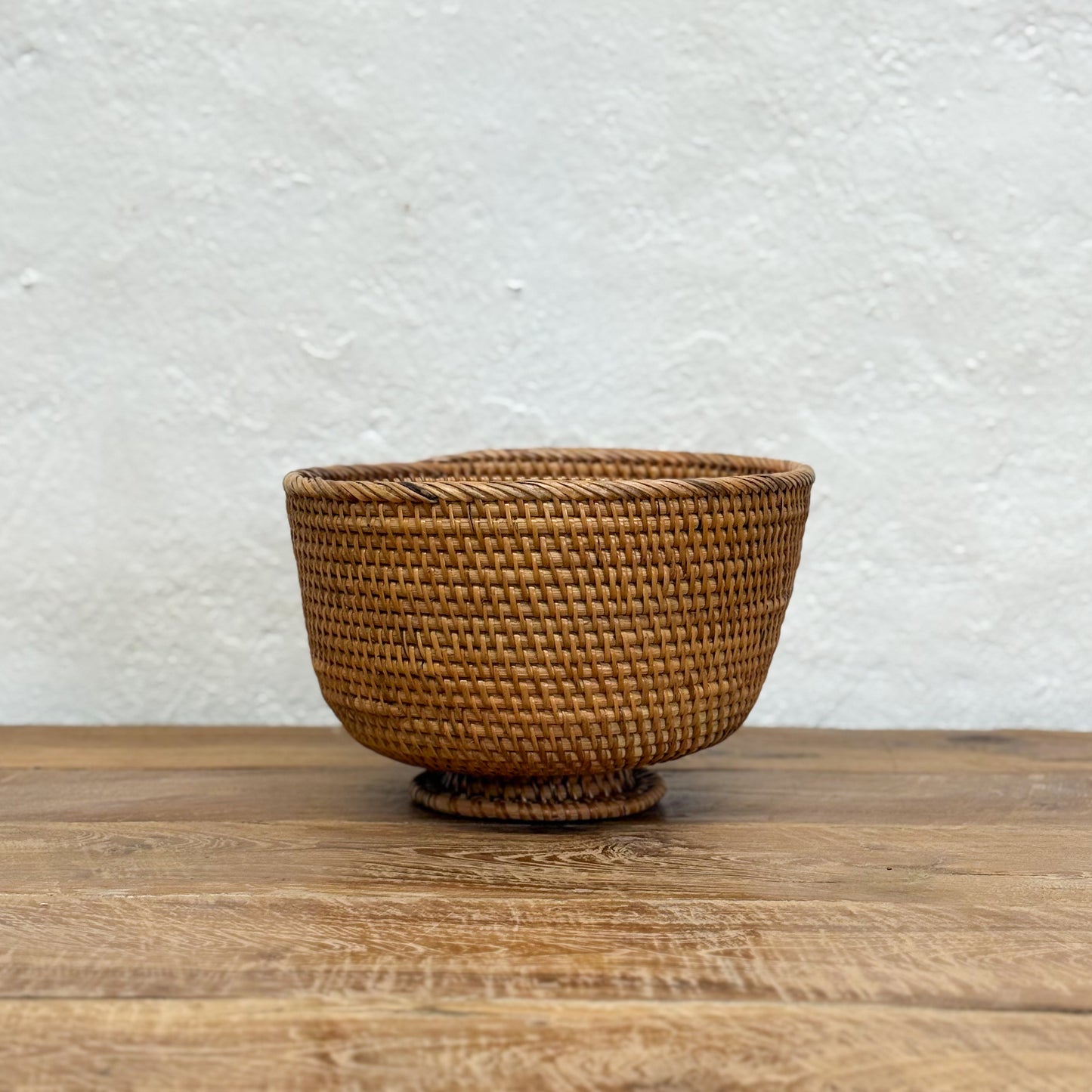 Woven basket on a wooden surface with a white textured wall background