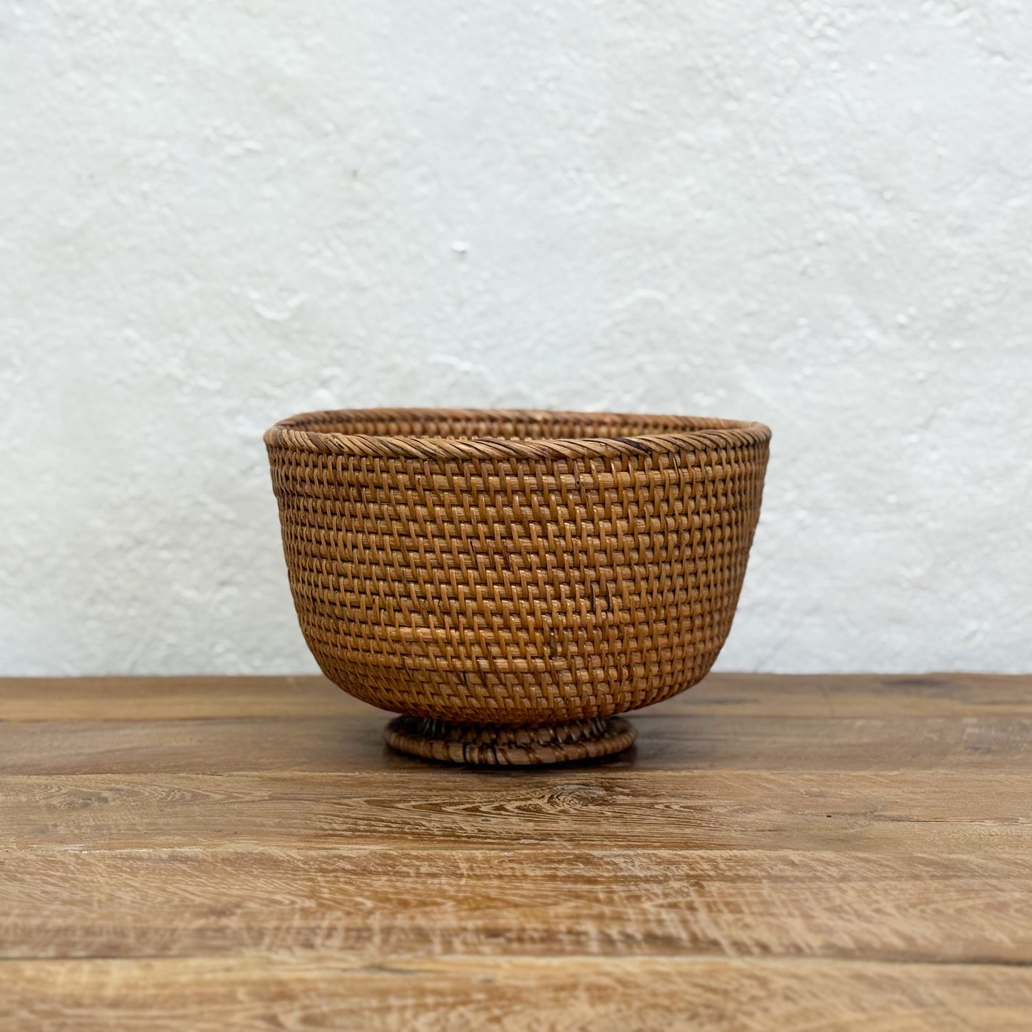 Woven brown basket on a wooden surface with a textured white wall background