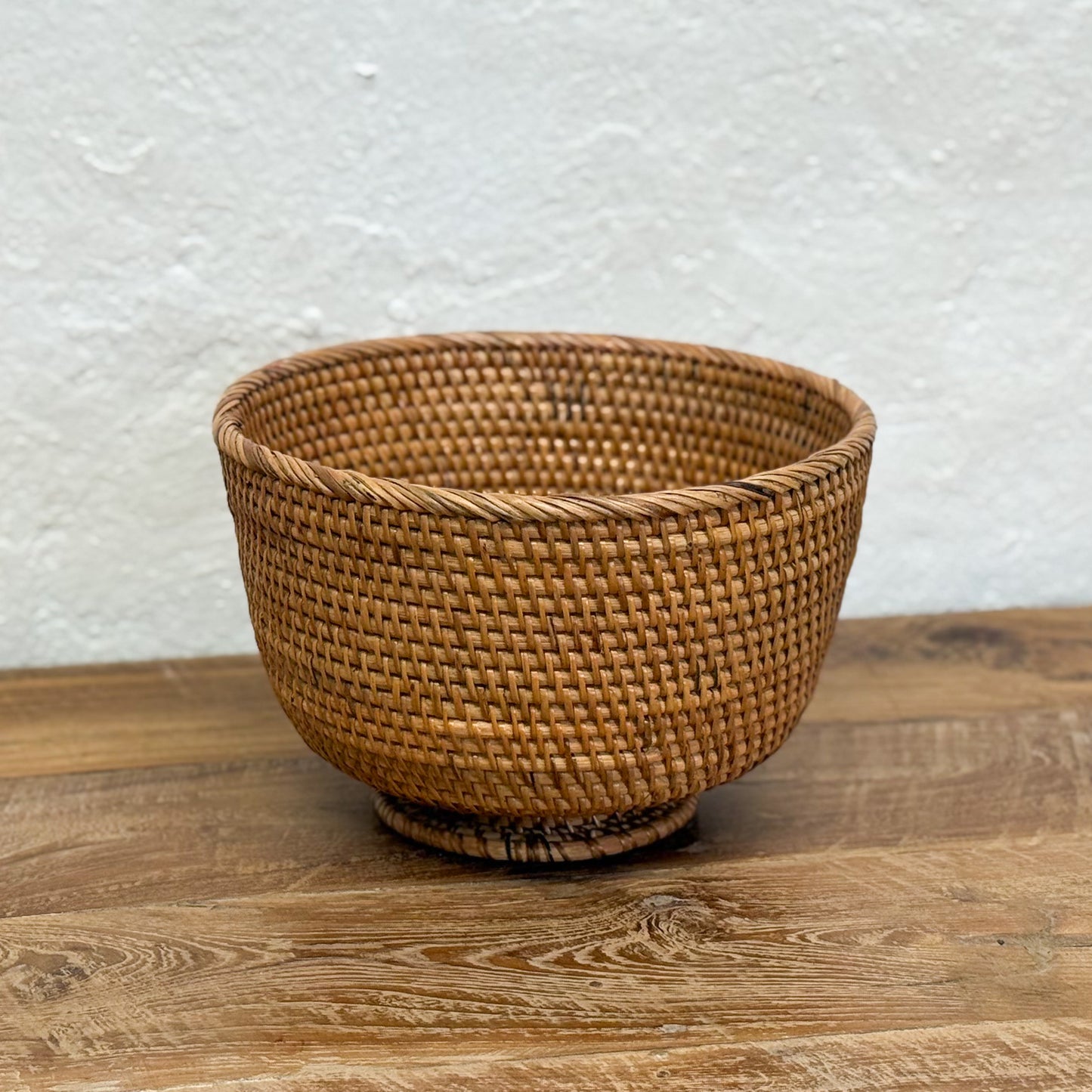 Woven brown basket on a wooden surface with a white textured wall background