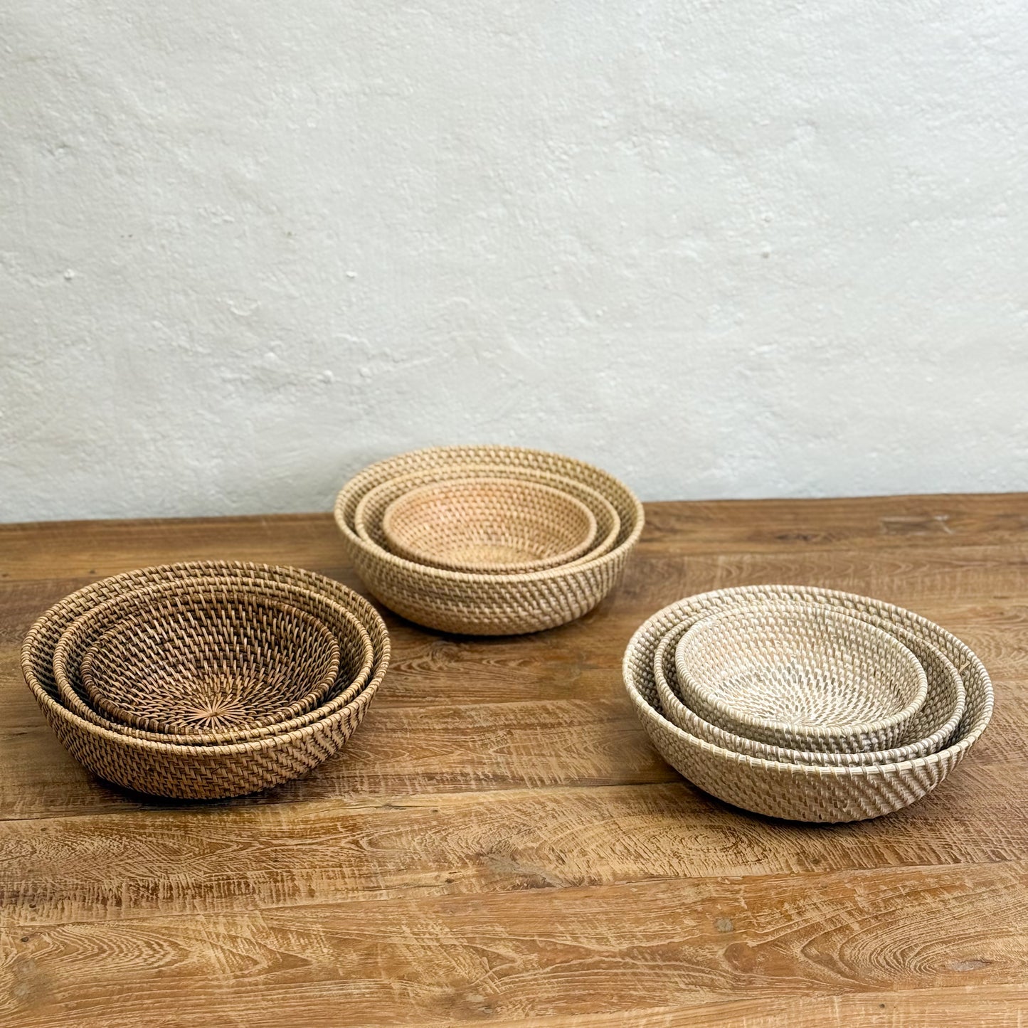 Set of three woven baskets on a wooden surface with a light gray background