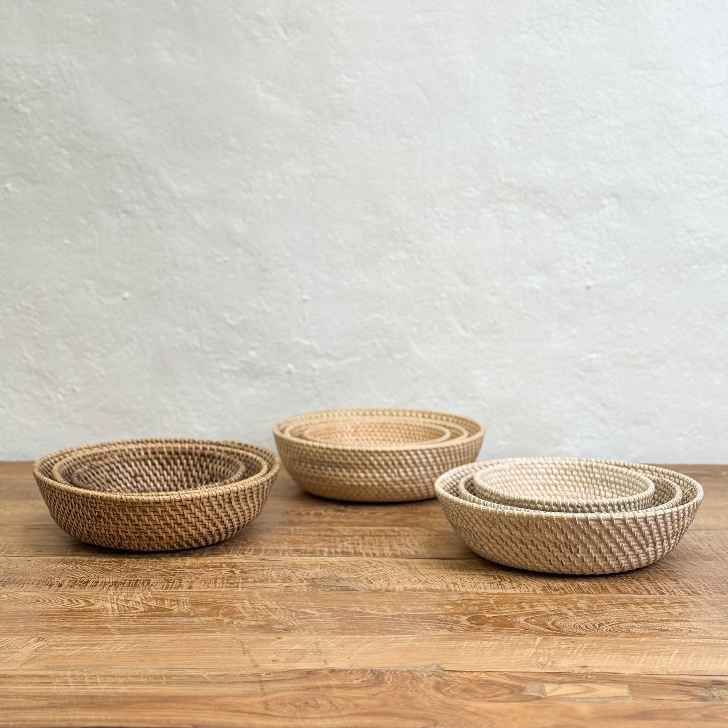Three woven baskets of different sizes on a wooden surface with a light gray textured wall background.
