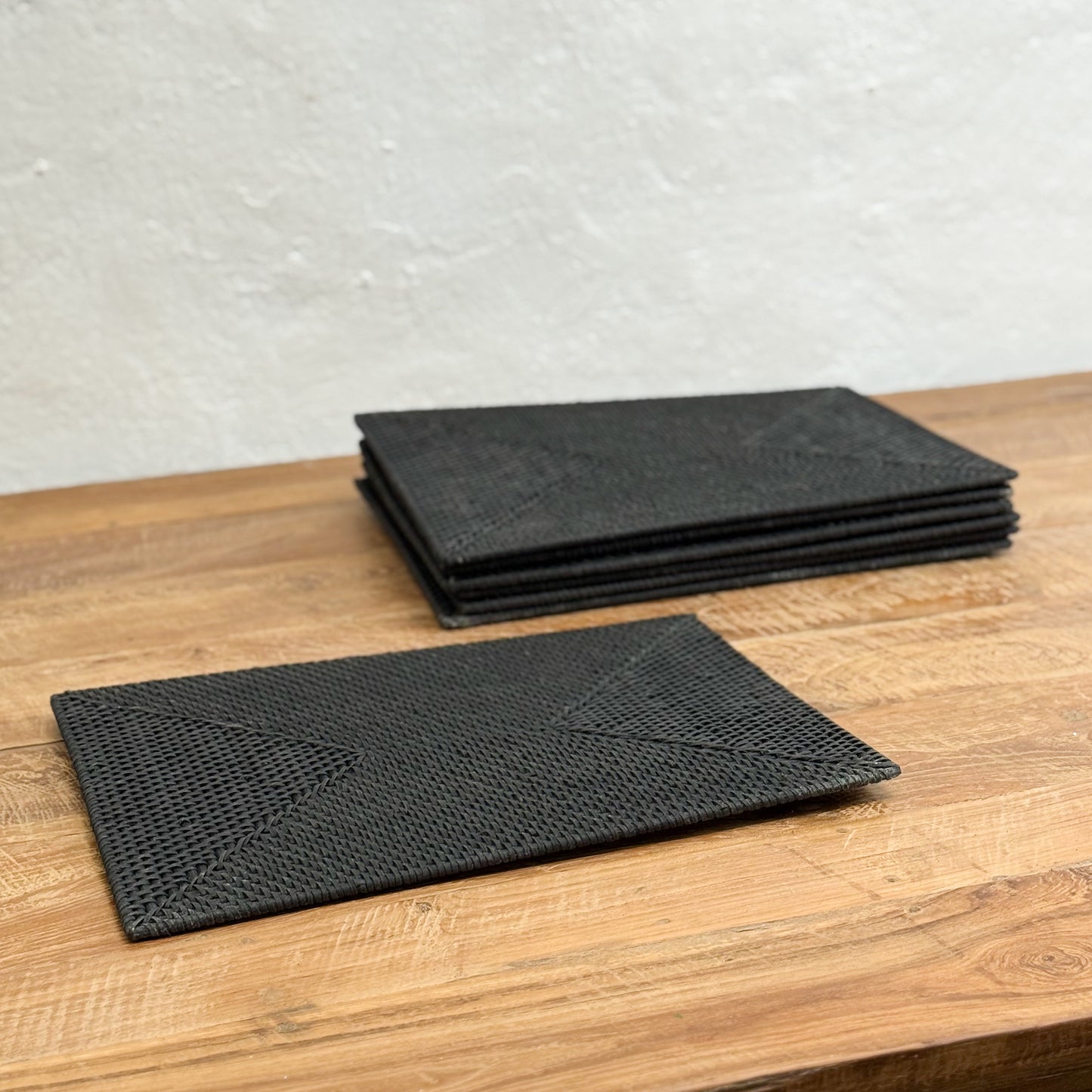 Set of black woven placemats on a wooden surface with a light gray background