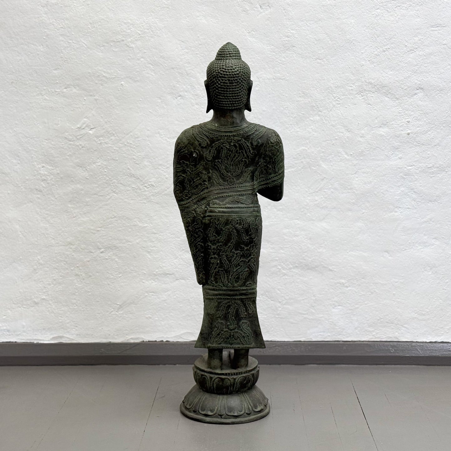 Statue of a figure in traditional attire against a white textured wall.
