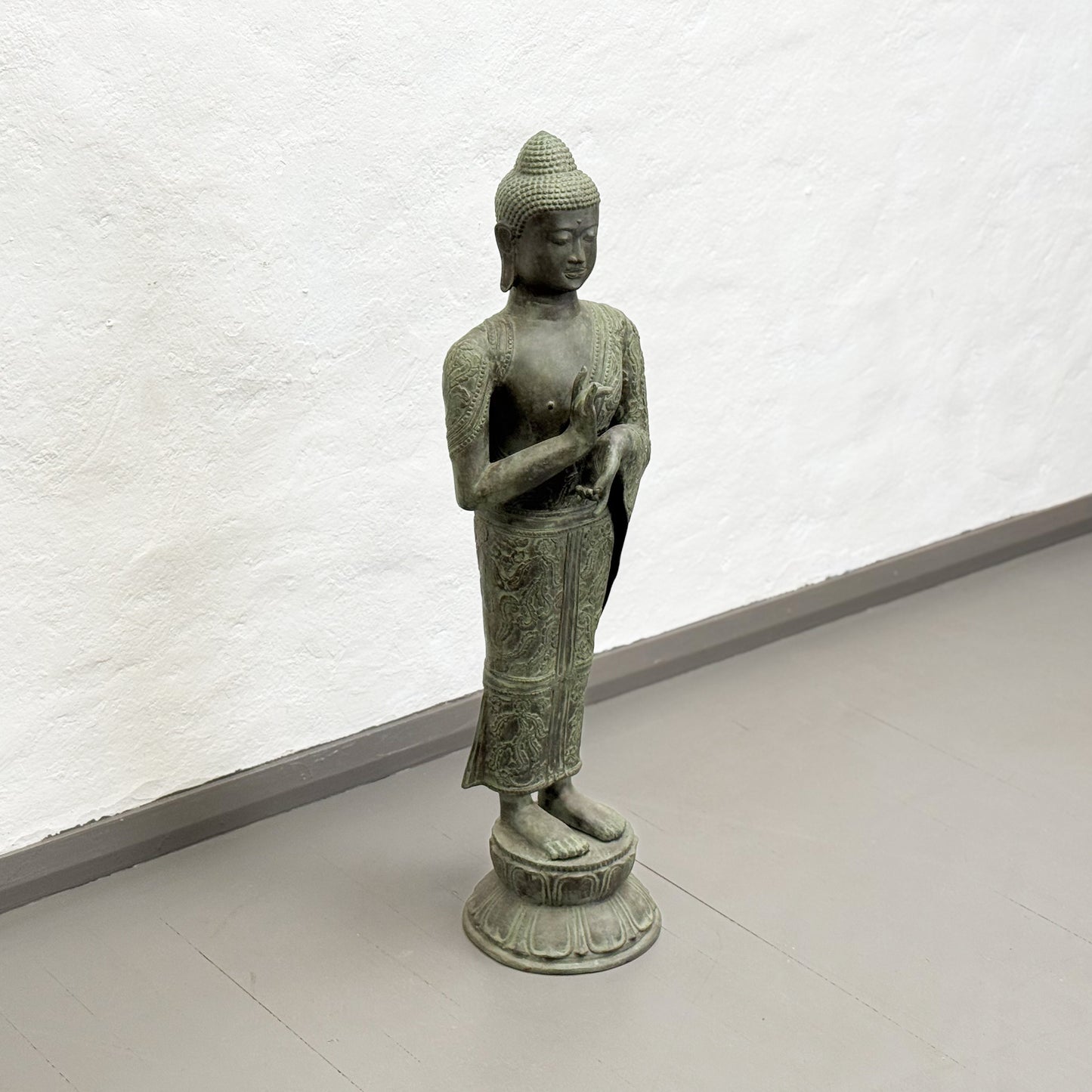Bronze statue of a standing Buddha on a white background