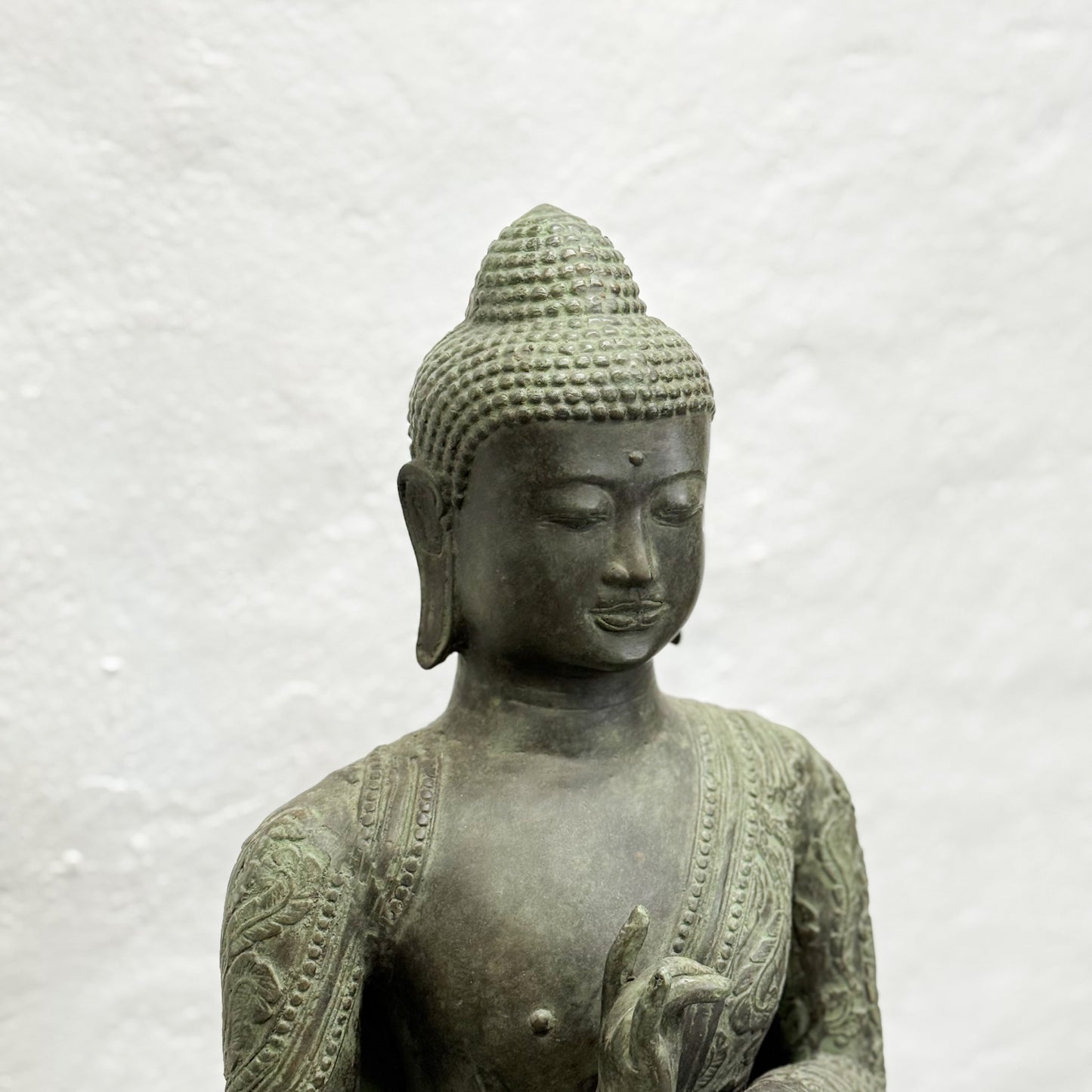 Bronze statue of a seated Buddha on a textured white background