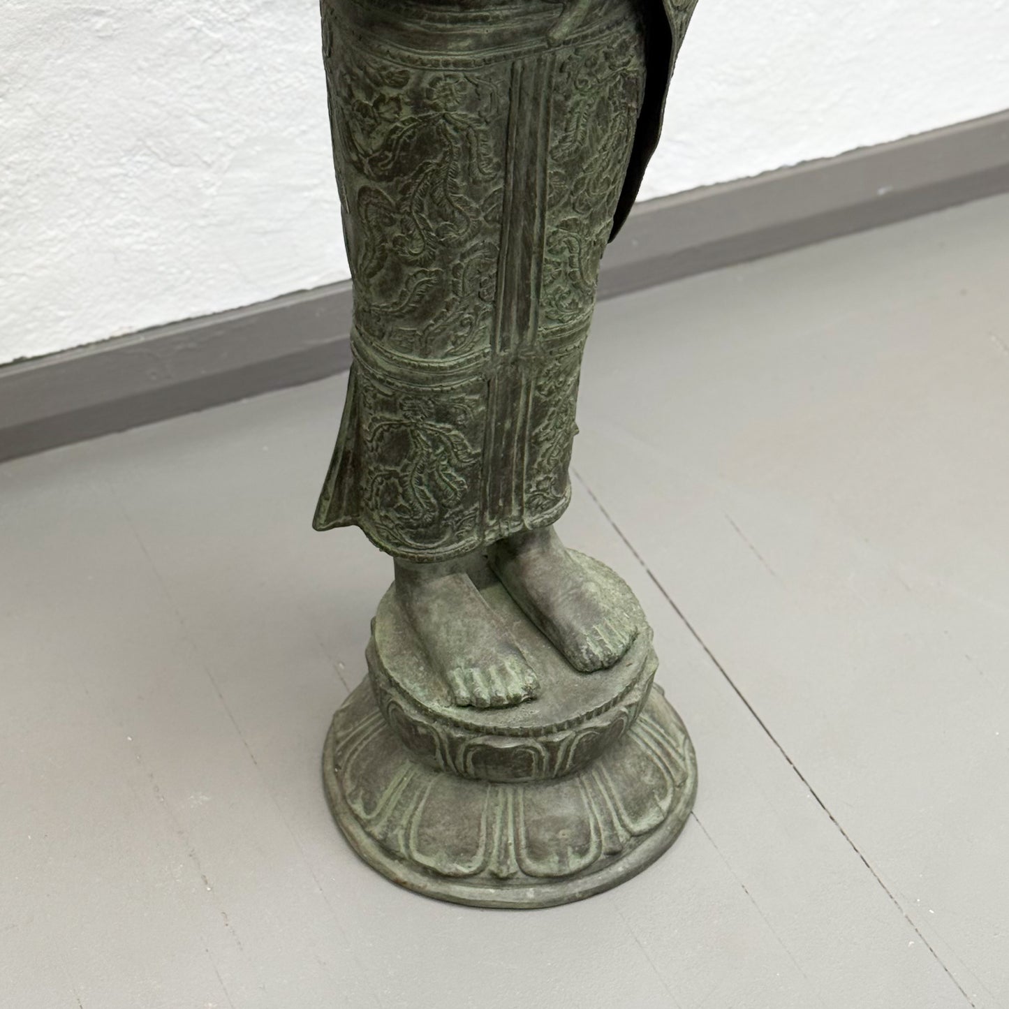 Bronze statue of a figure with detailed clothing on a white floor.