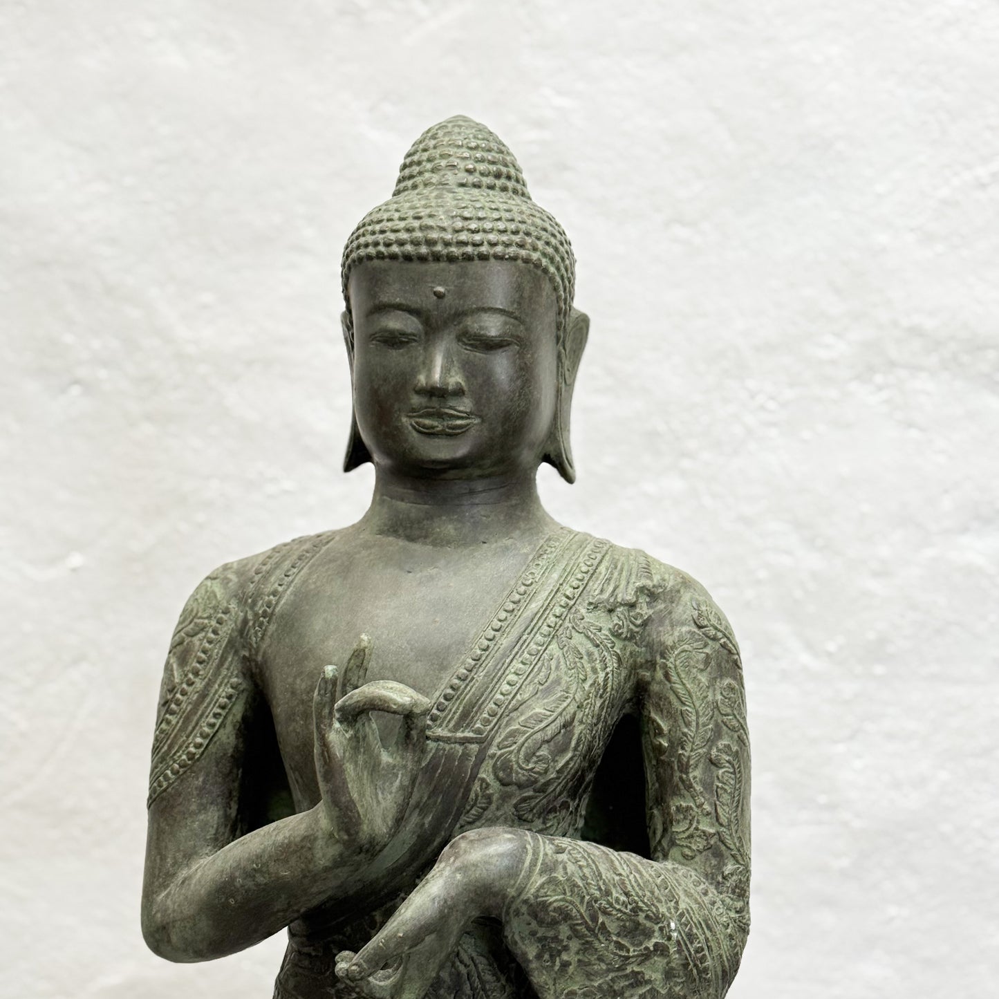 Bronze statue of a seated Buddha on a textured white background