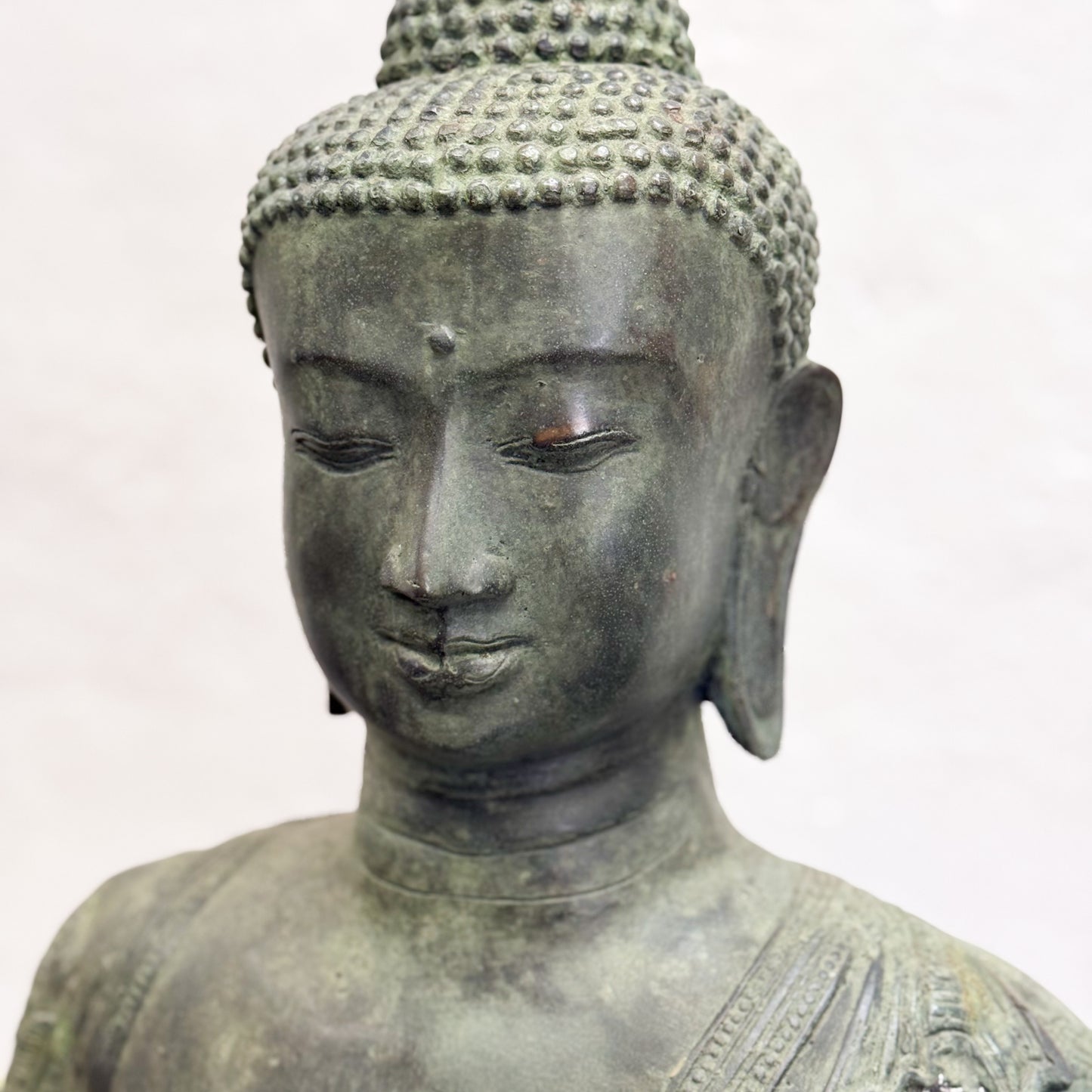 Bronze statue of a seated Buddha with detailed hair and clothing on a white background