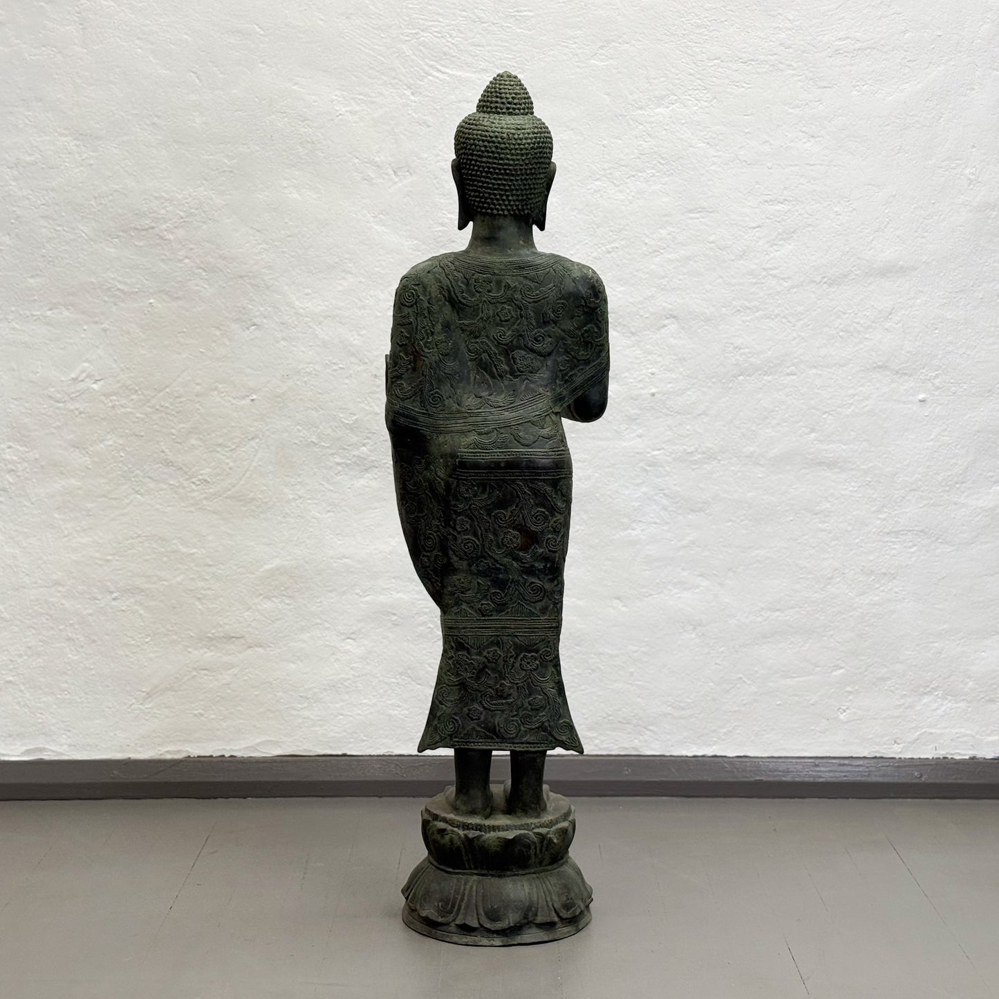 Statue of a Buddha figure against a textured white wall.