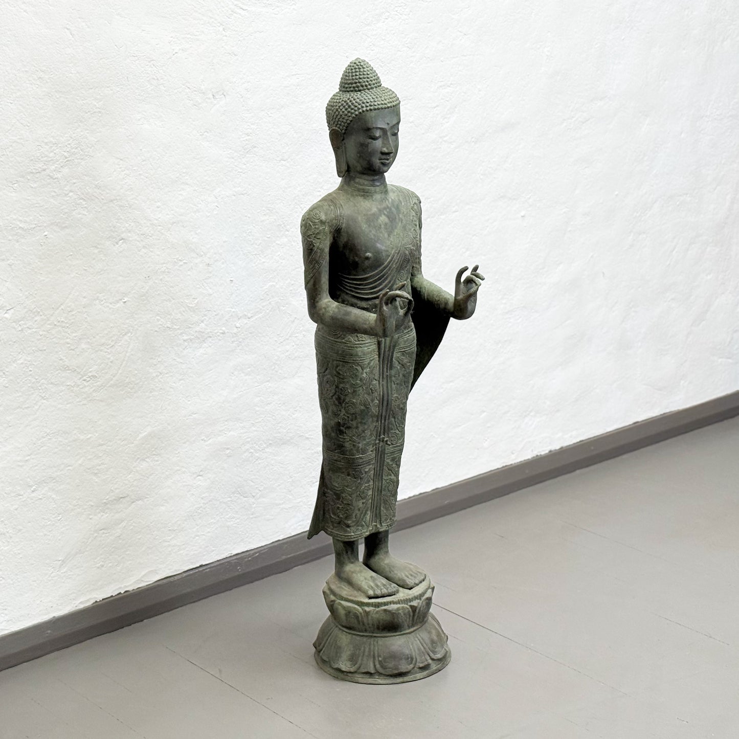 Bronze statue of a standing Buddha on a white background