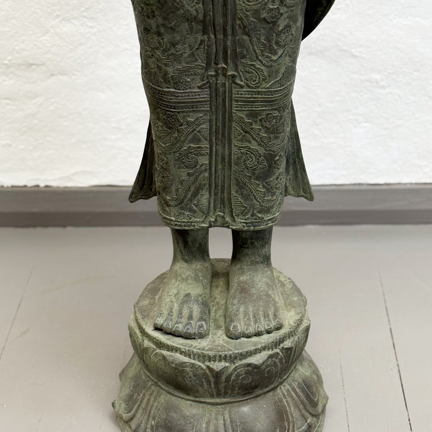 Bronze statue of a figure with detailed clothing and feet on a white background