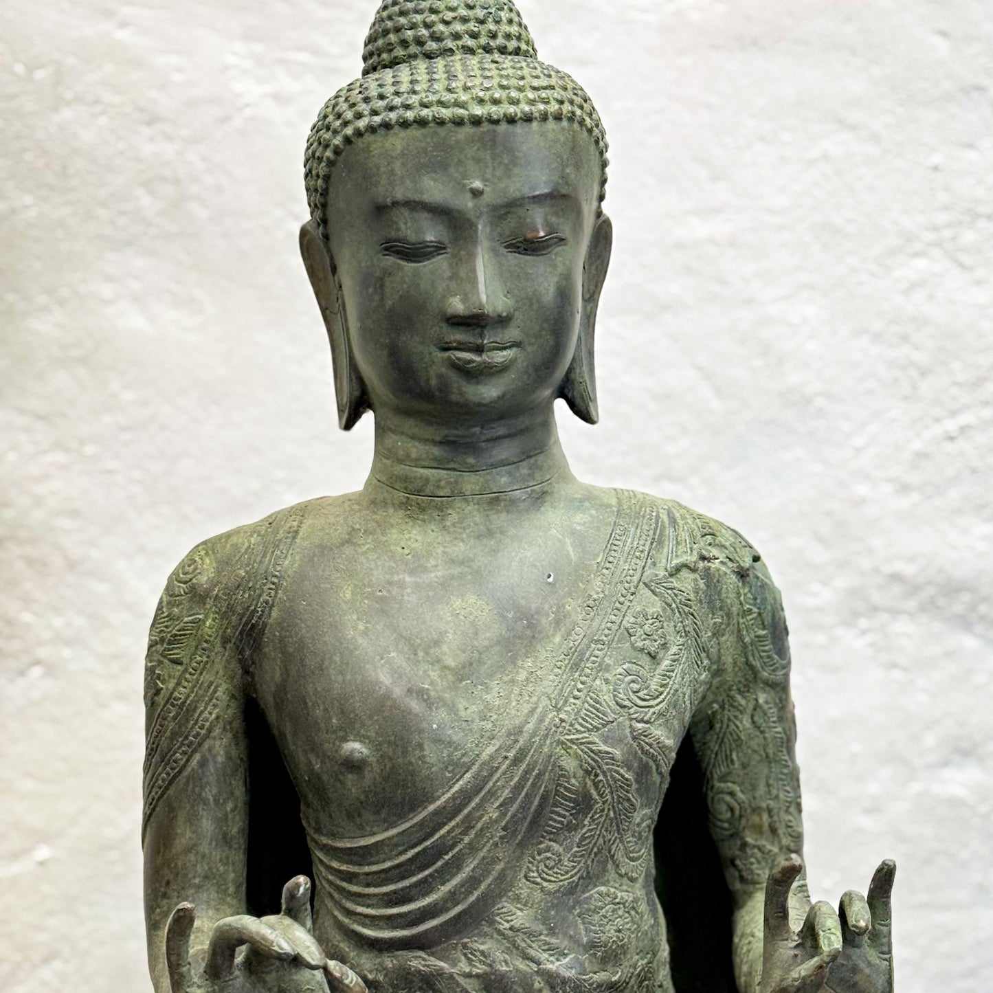 Bronze statue of a seated Buddha on a textured white background