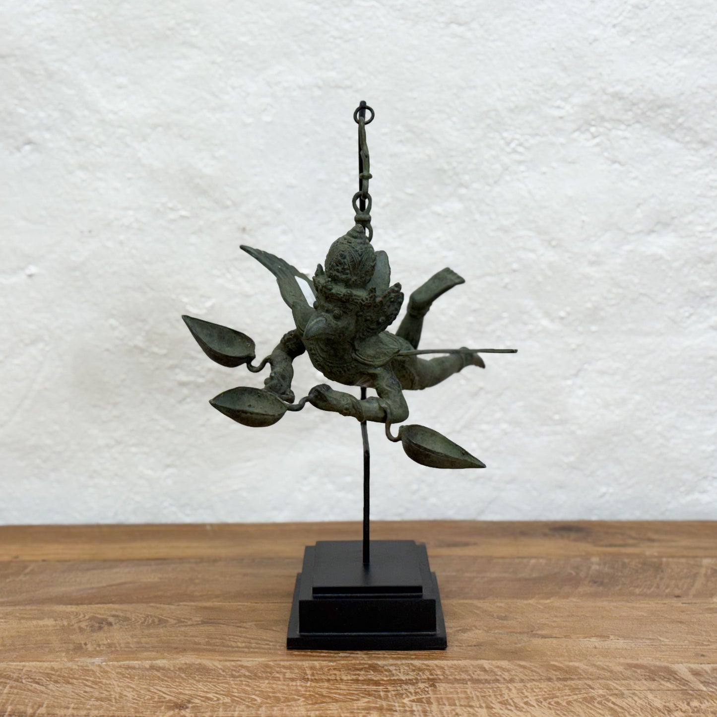 Bronze statue of a deity on a stand against a textured white wall.