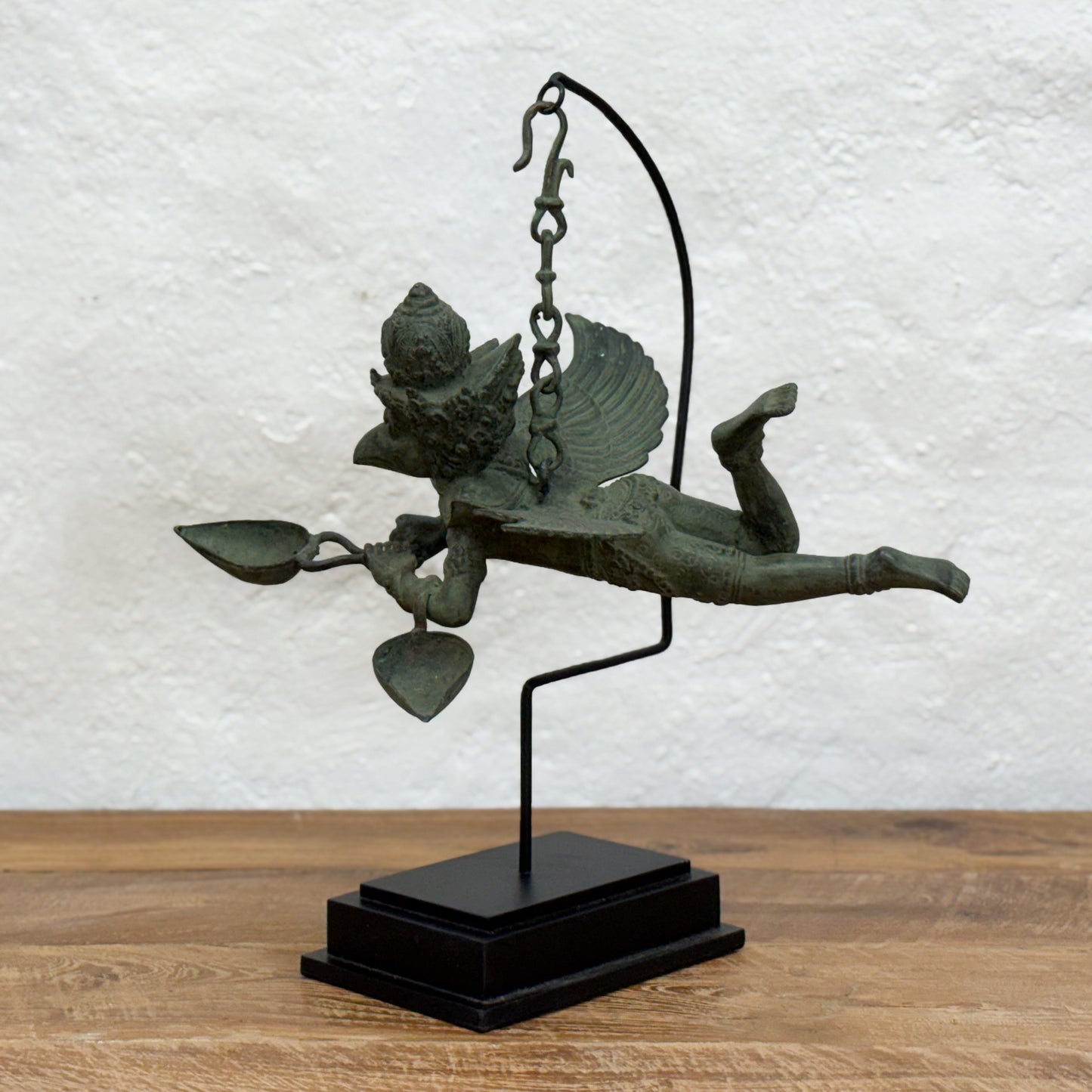 Bronze sculpture of a winged figure on a wooden surface with a white textured wall background