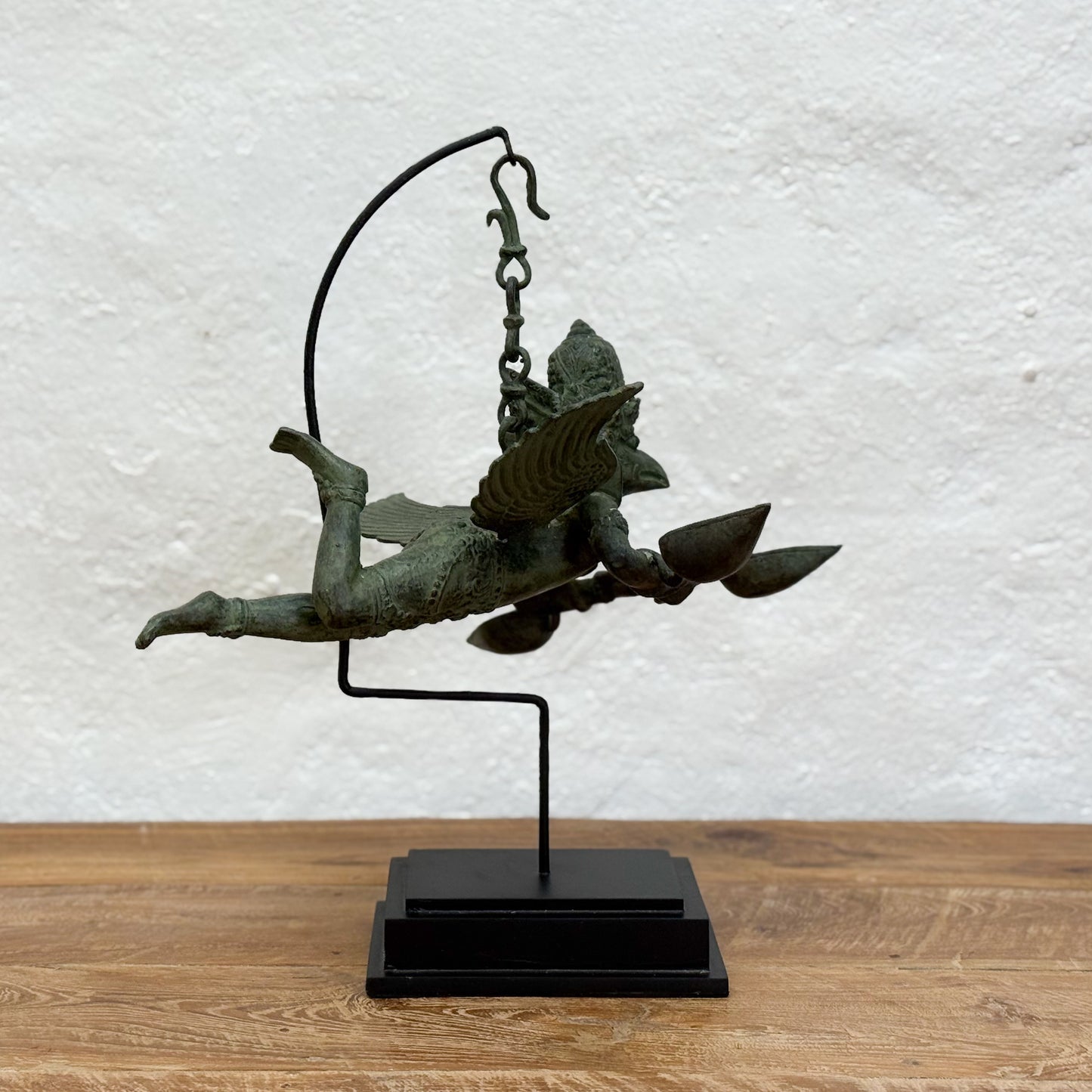 Bronze statue of a winged figure on a stand against a textured white wall.