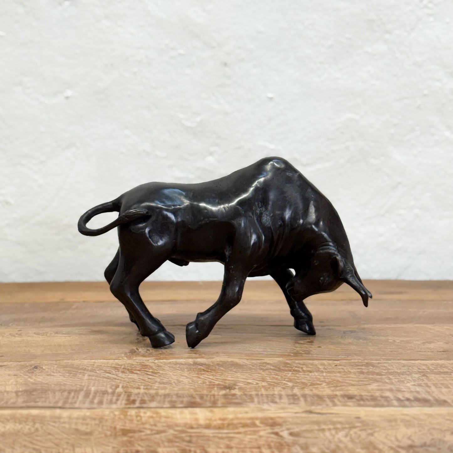 Bronze bull sculpture on a wooden surface with a textured white wall background