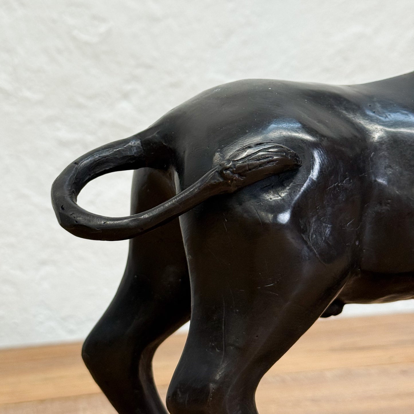 Close-up of a black bull statue with a textured white wall background