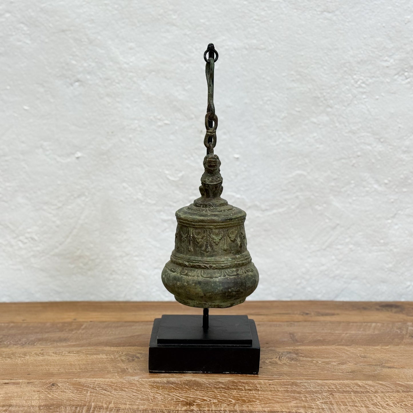 Bronze bell on a stand against a textured white wall