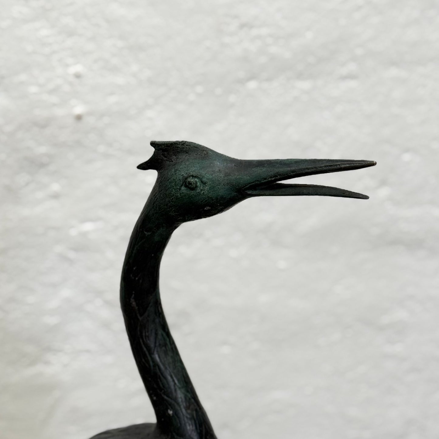Bronze sculpture of a heron on a textured gray background