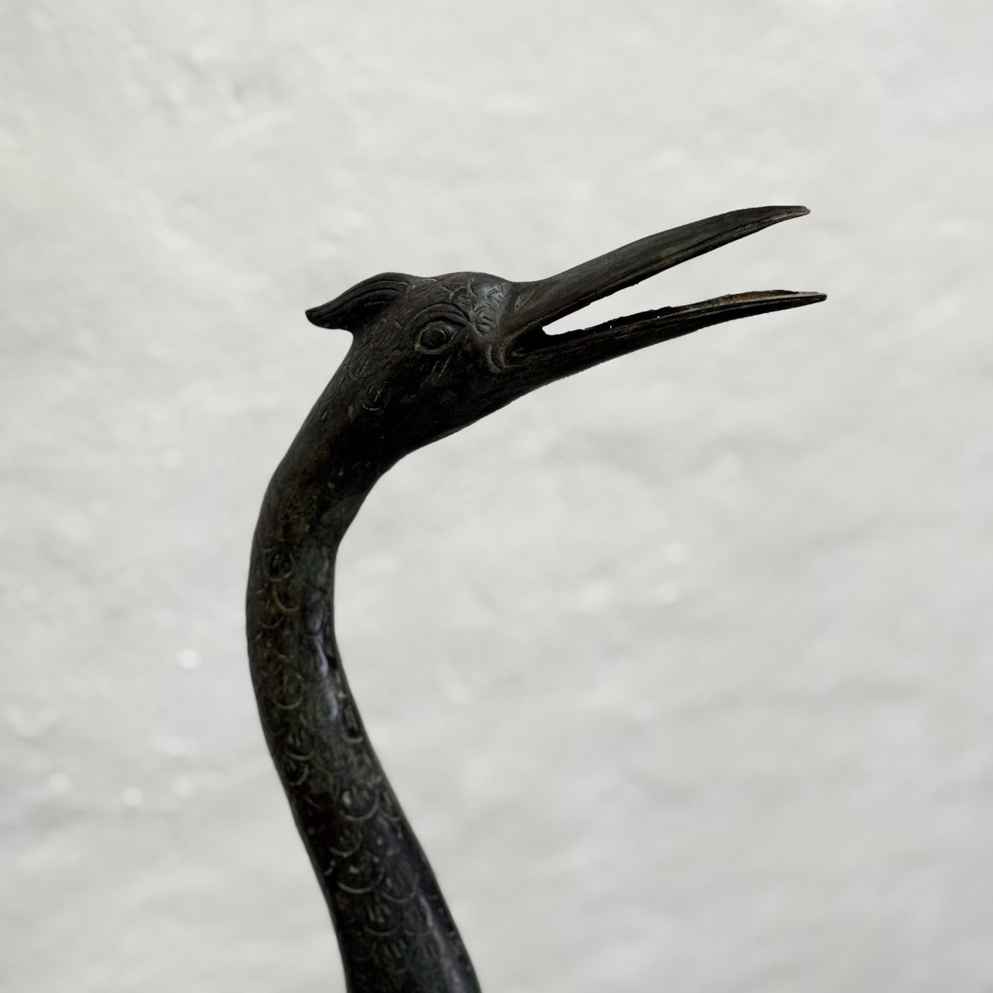 Bronze sculpture of a crane with detailed carvings on a light gray background
