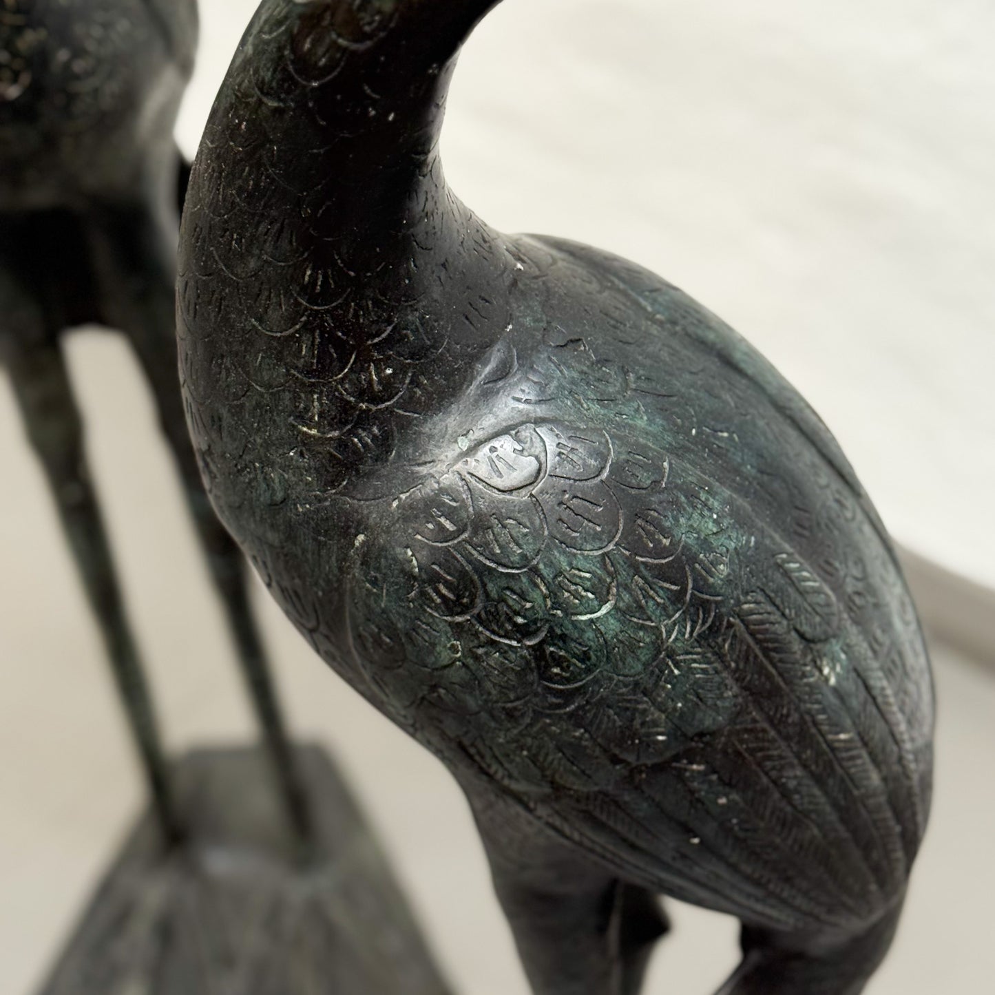 Bronze statue of a crane with detailed feathers on a plain background