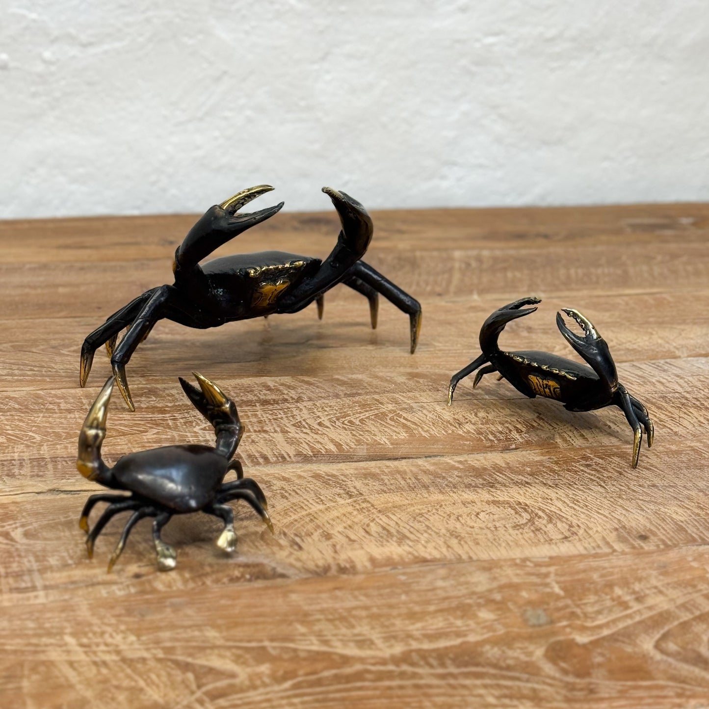 Three black crab figurines with gold accents on a wooden surface.