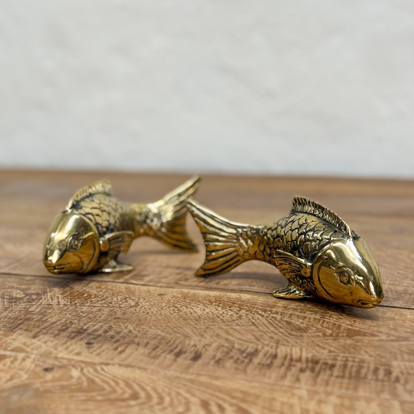 Two gold fish figurines on a wooden surface with a neutral background