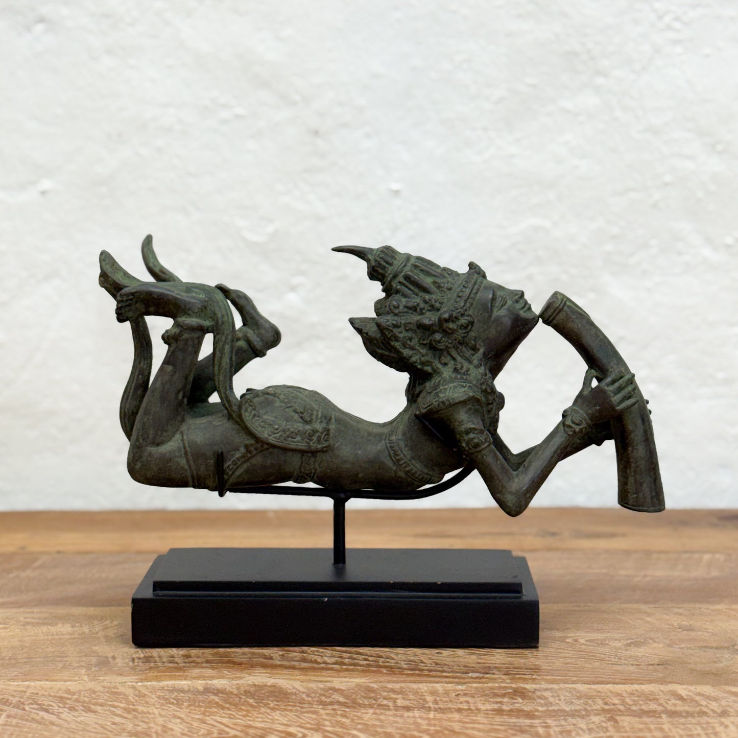 Bronze statue of a reclining figure on a wooden surface with a white textured wall background
