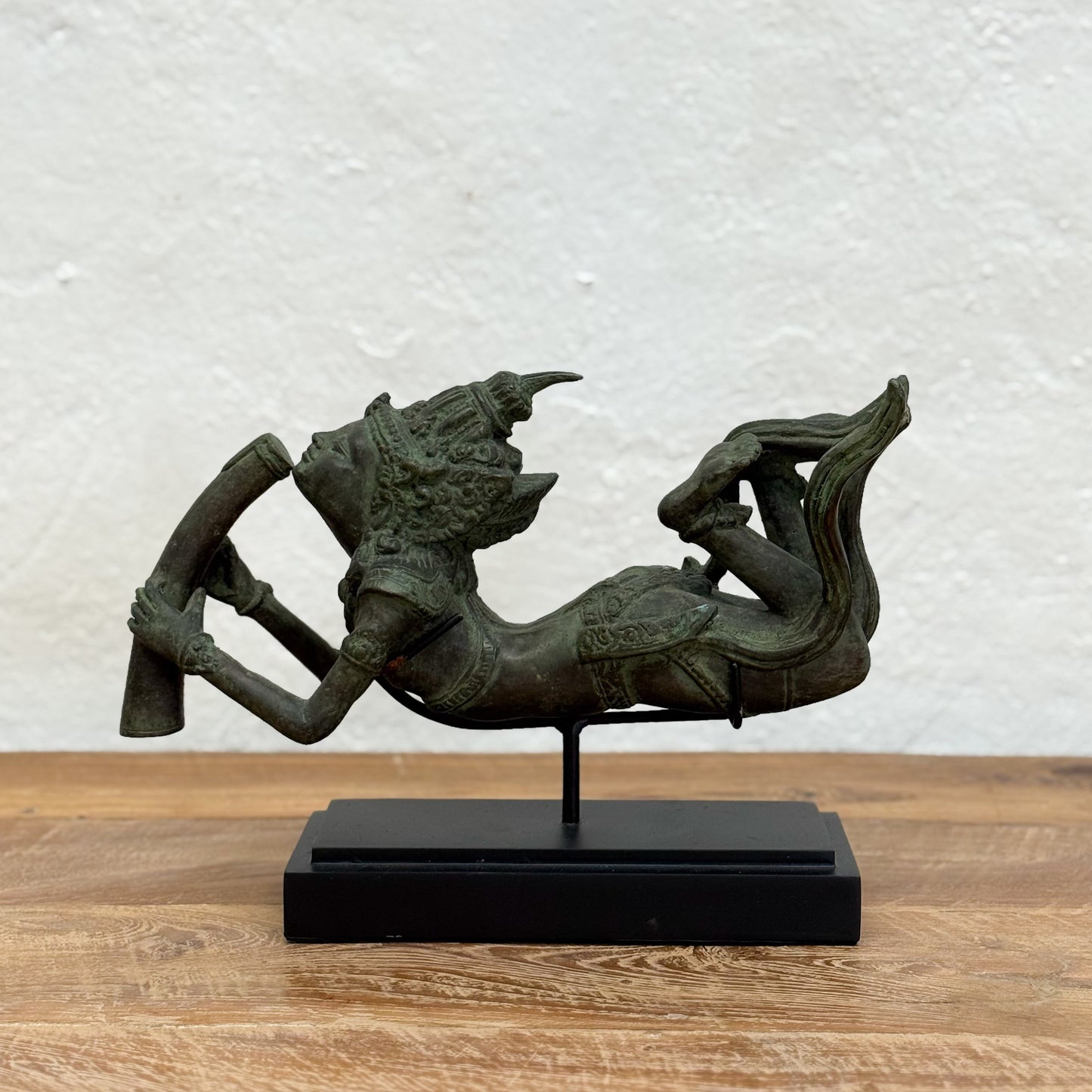 Bronze sculpture of a mythical creature on a wooden surface with a white textured wall background