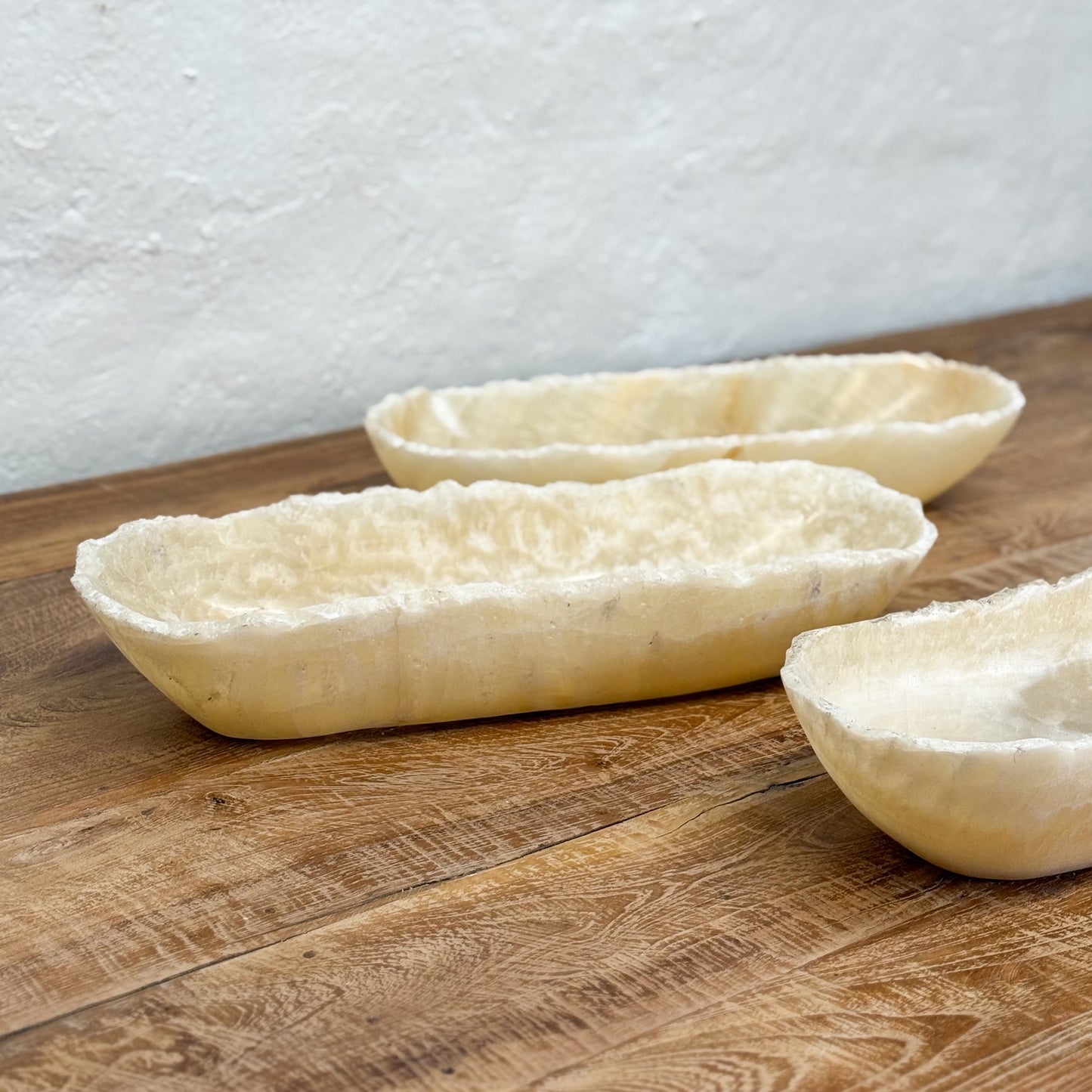 Three unbaked bread loaves on a wooden surface with a white textured wall background.