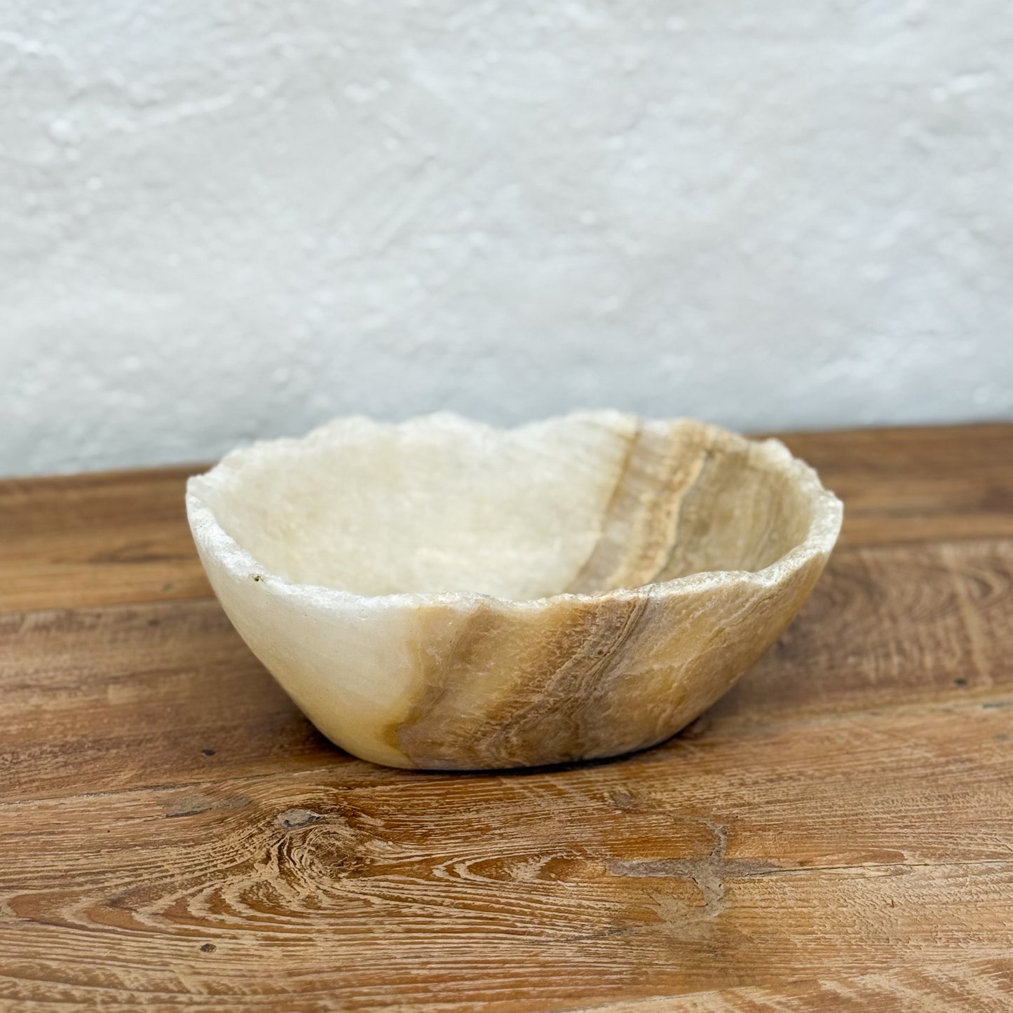 Decorative stone bowl on a wooden surface with a textured white wall background