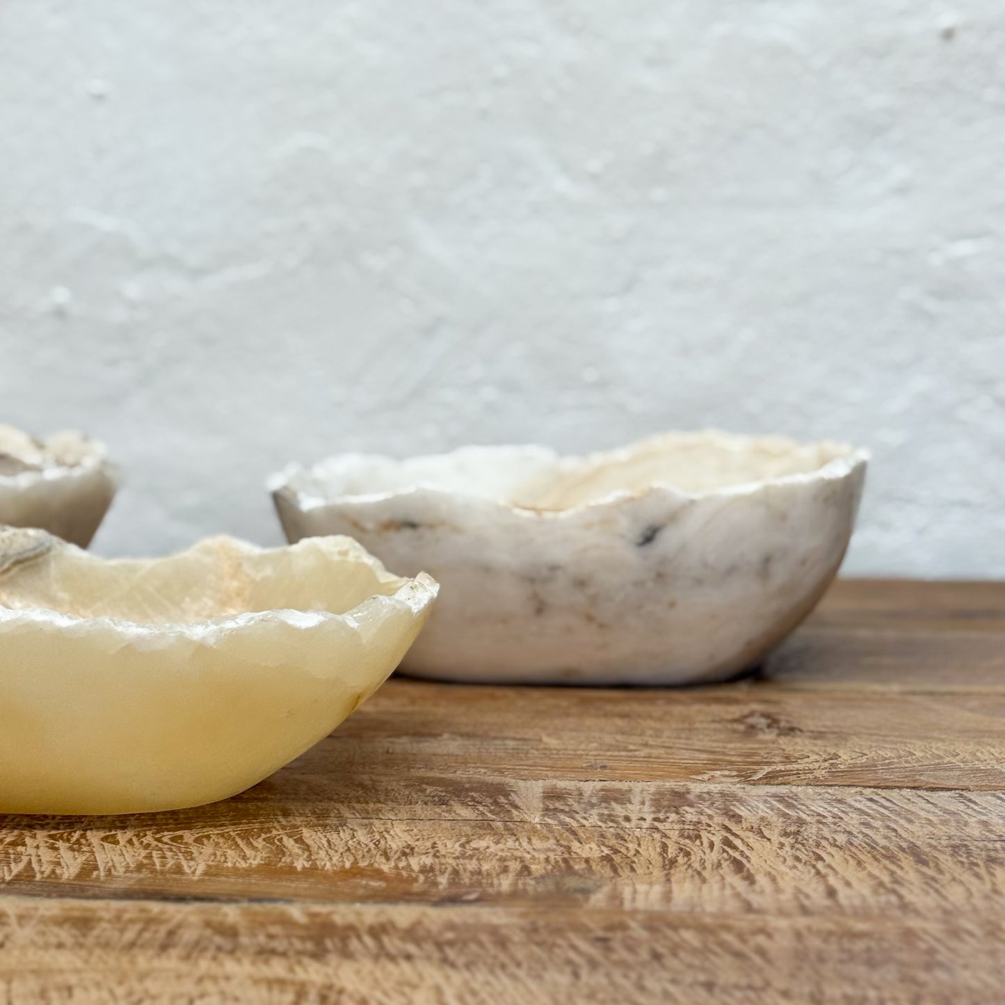 Three stone bowls on a wooden surface with a light gray textured wall in the background