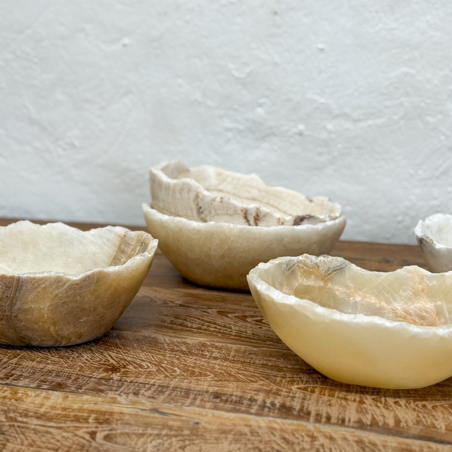 Three stone bowls on a wooden surface with a light gray textured wall in the background.