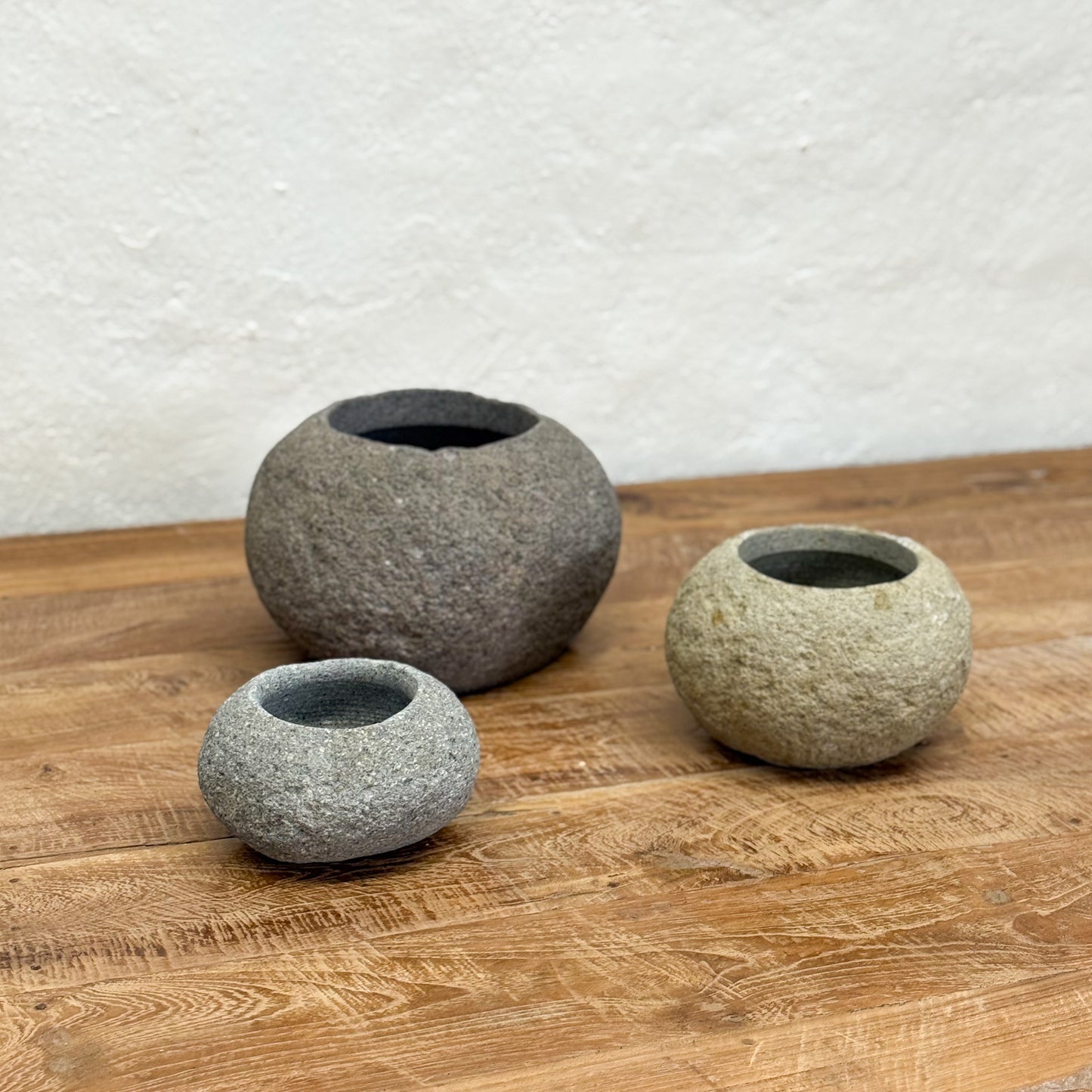 Three stone-like bowls on a wooden surface with a textured white wall background
