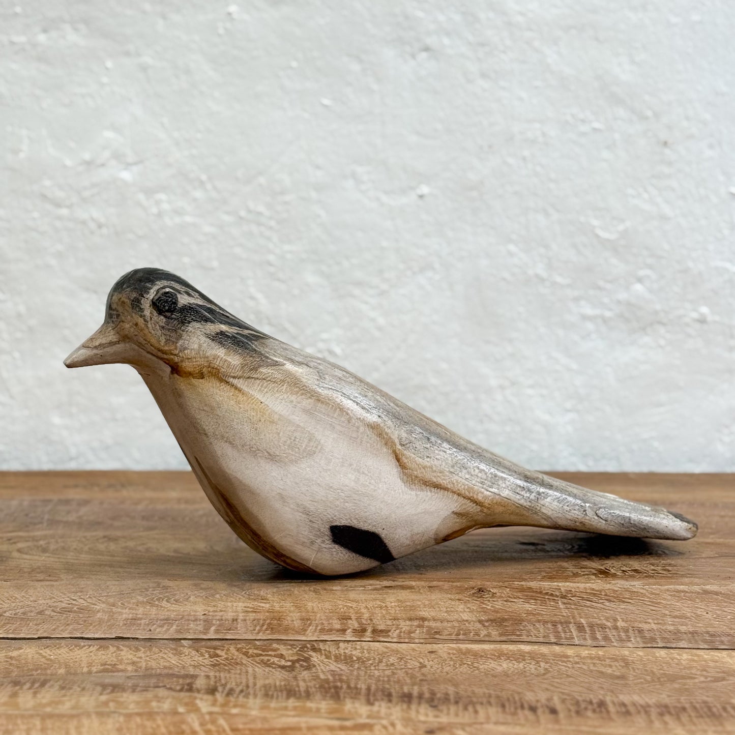 Decorative bird sculpture on a wooden surface with a textured white wall background