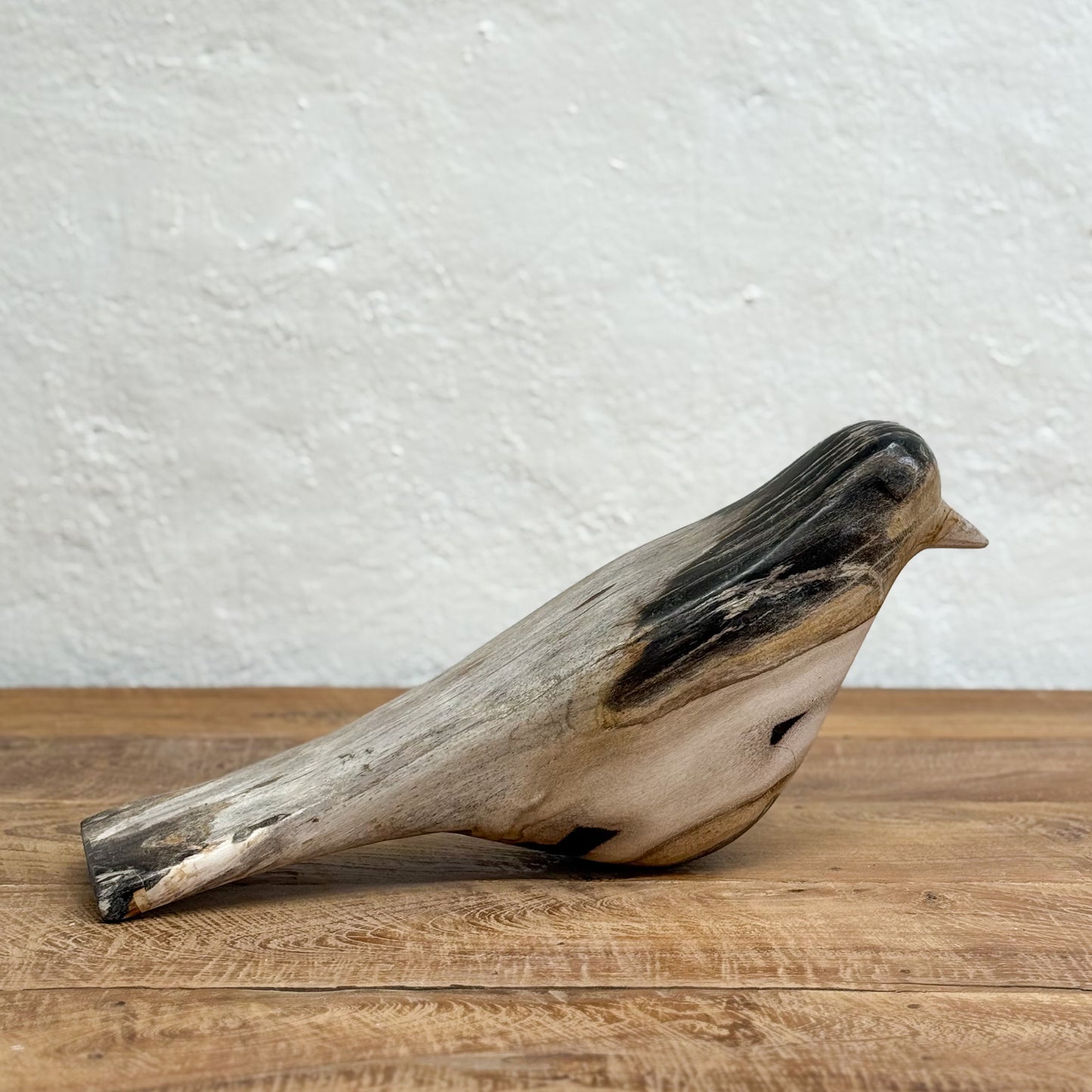 Wooden bird sculpture on a wooden surface with a white textured wall background