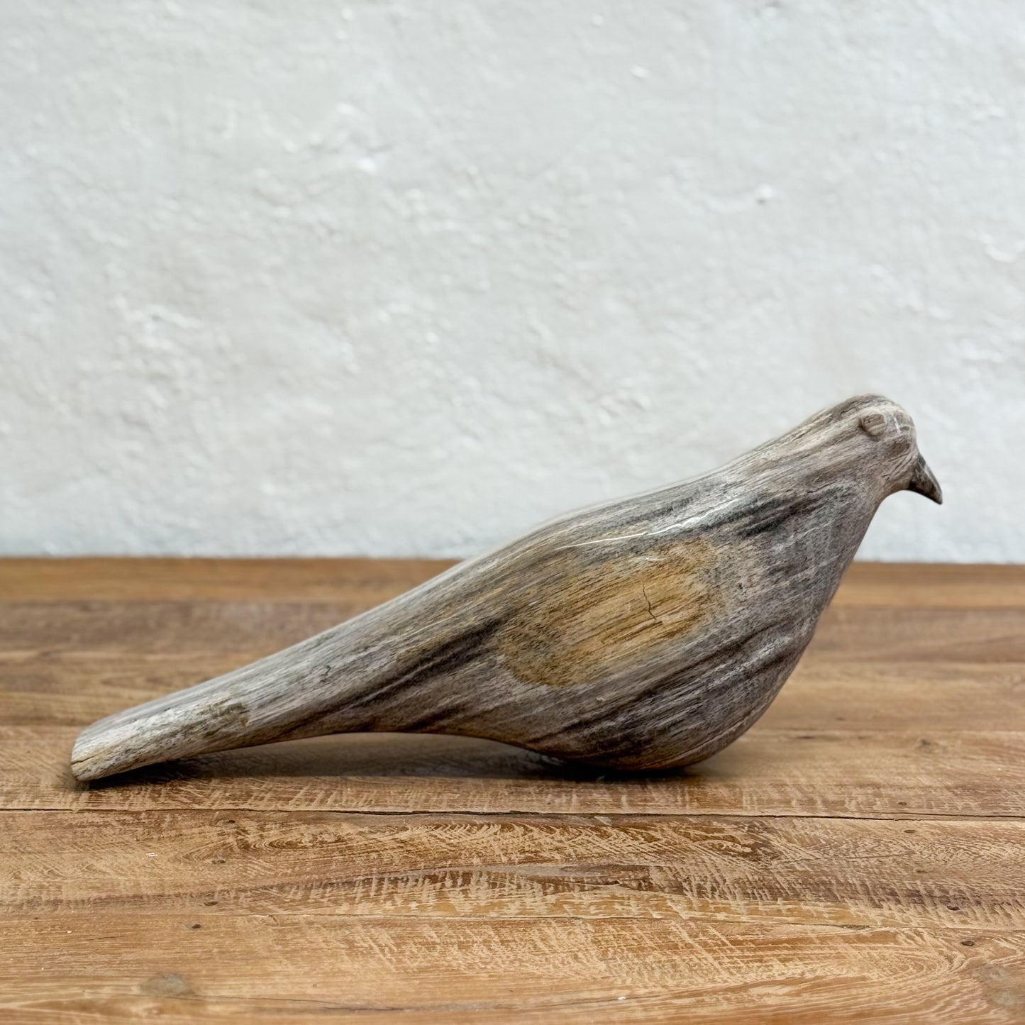 Wooden bird sculpture on a wooden surface with a white textured wall background