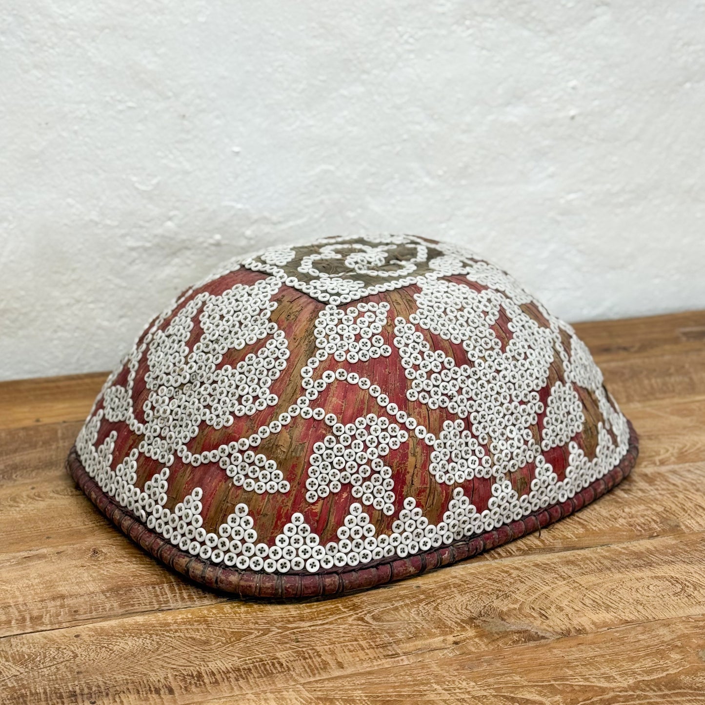 Decorative dome-shaped object with intricate white beadwork on a wooden surface.