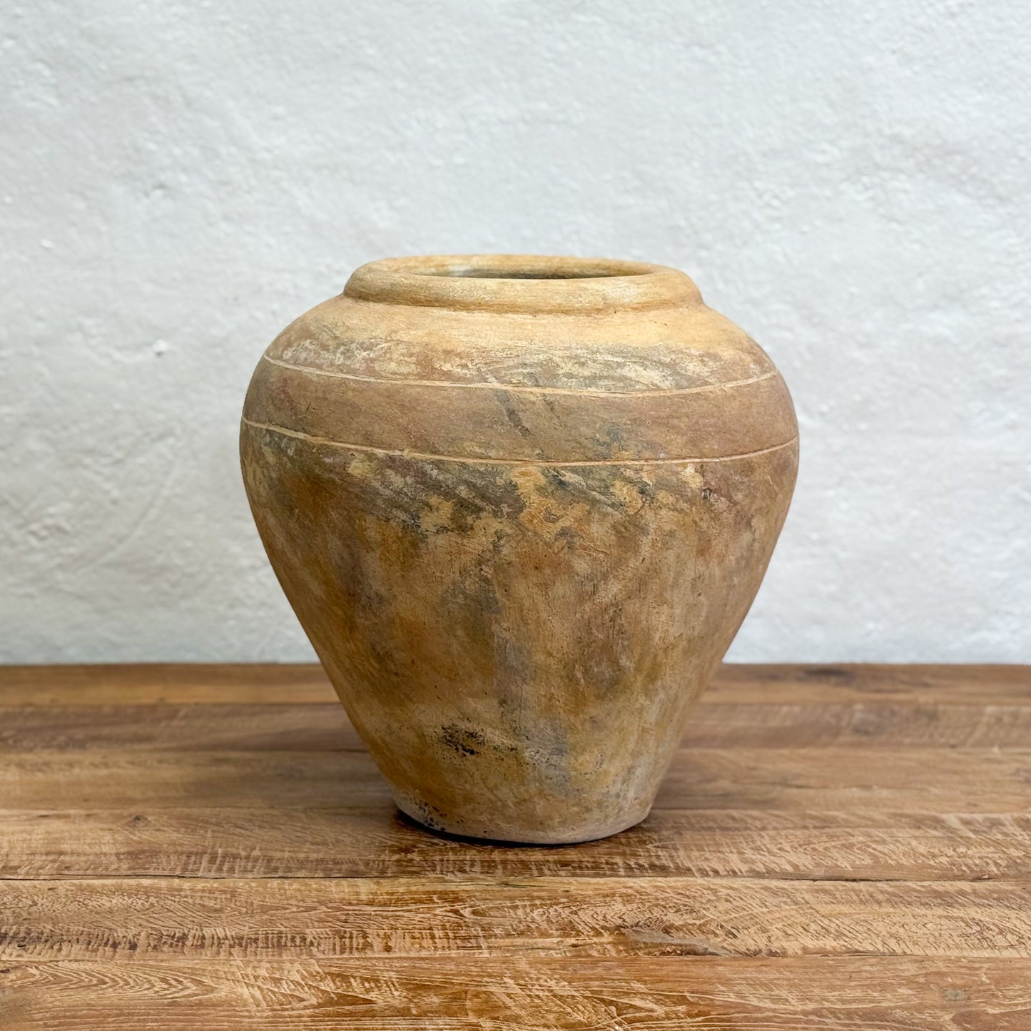 Vintage stone jar on a wooden surface with a textured white wall background
