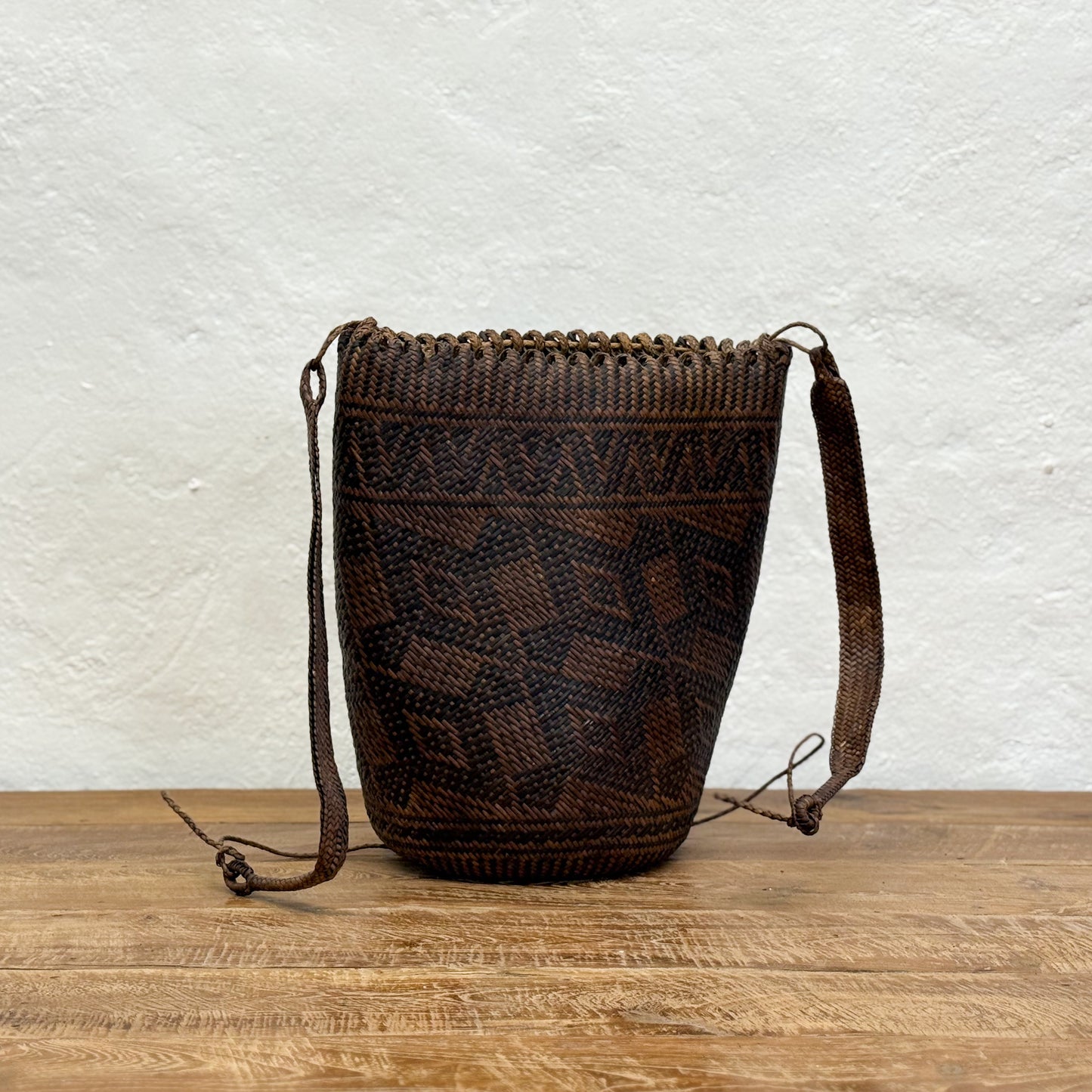 Woven brown bag with a geometric pattern on a wooden surface and white textured wall background