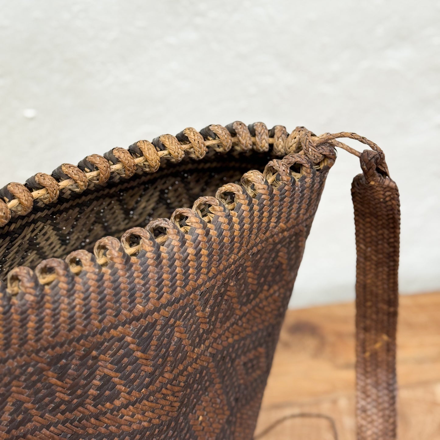 Close-up of a woven basket with intricate patterns and a tassel on a wooden surface.