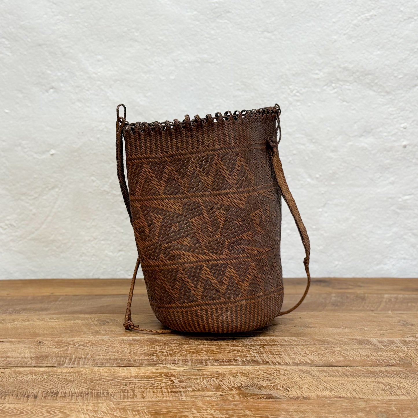 Brown woven bag with drawstring on a wooden surface and light gray textured background