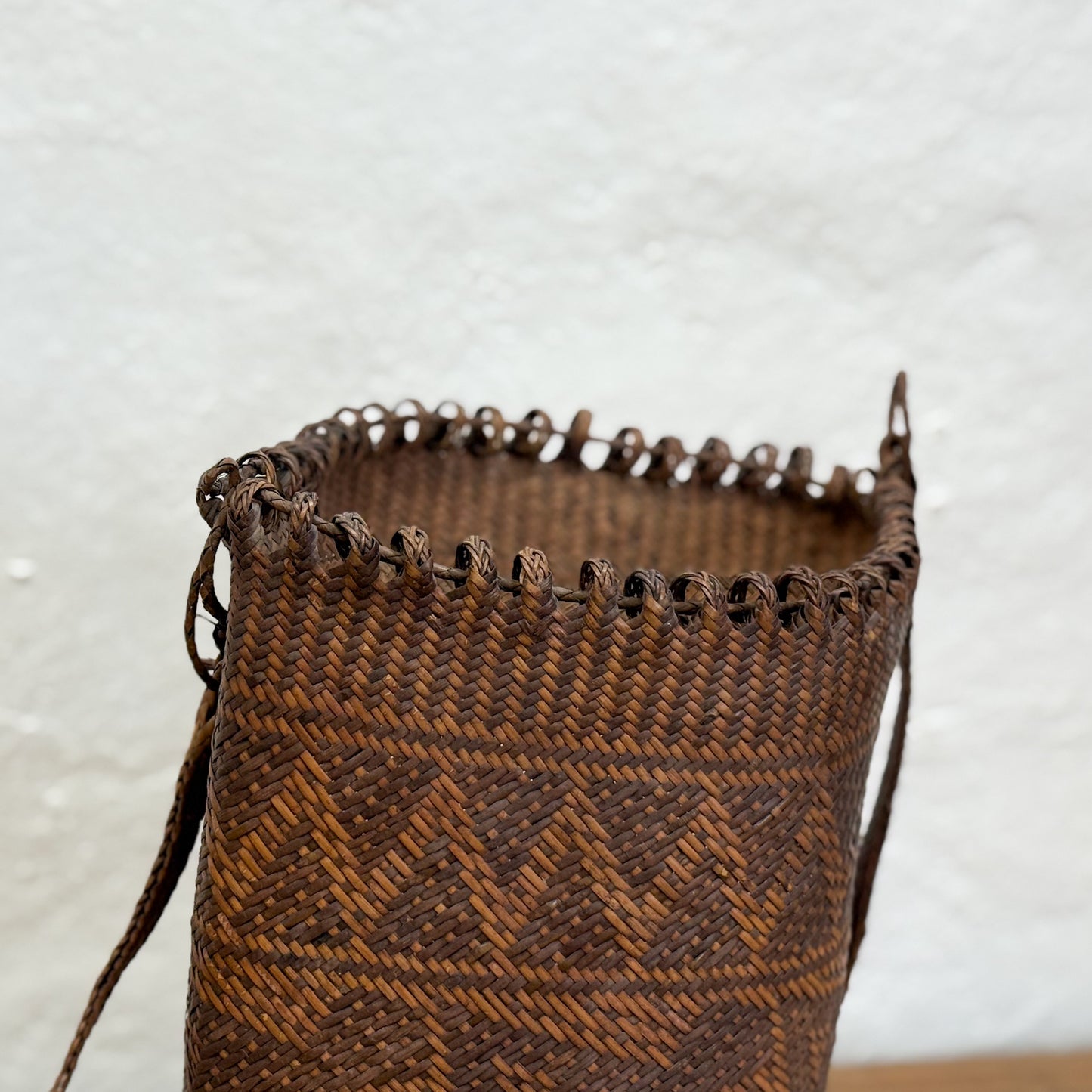 Brown woven basket with geometric pattern on a light gray background