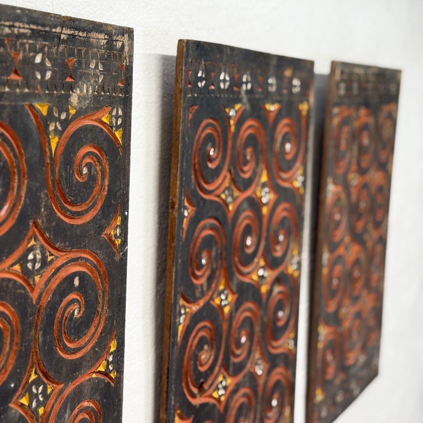 Three decorative wooden panels with intricate patterns on a white wall.
