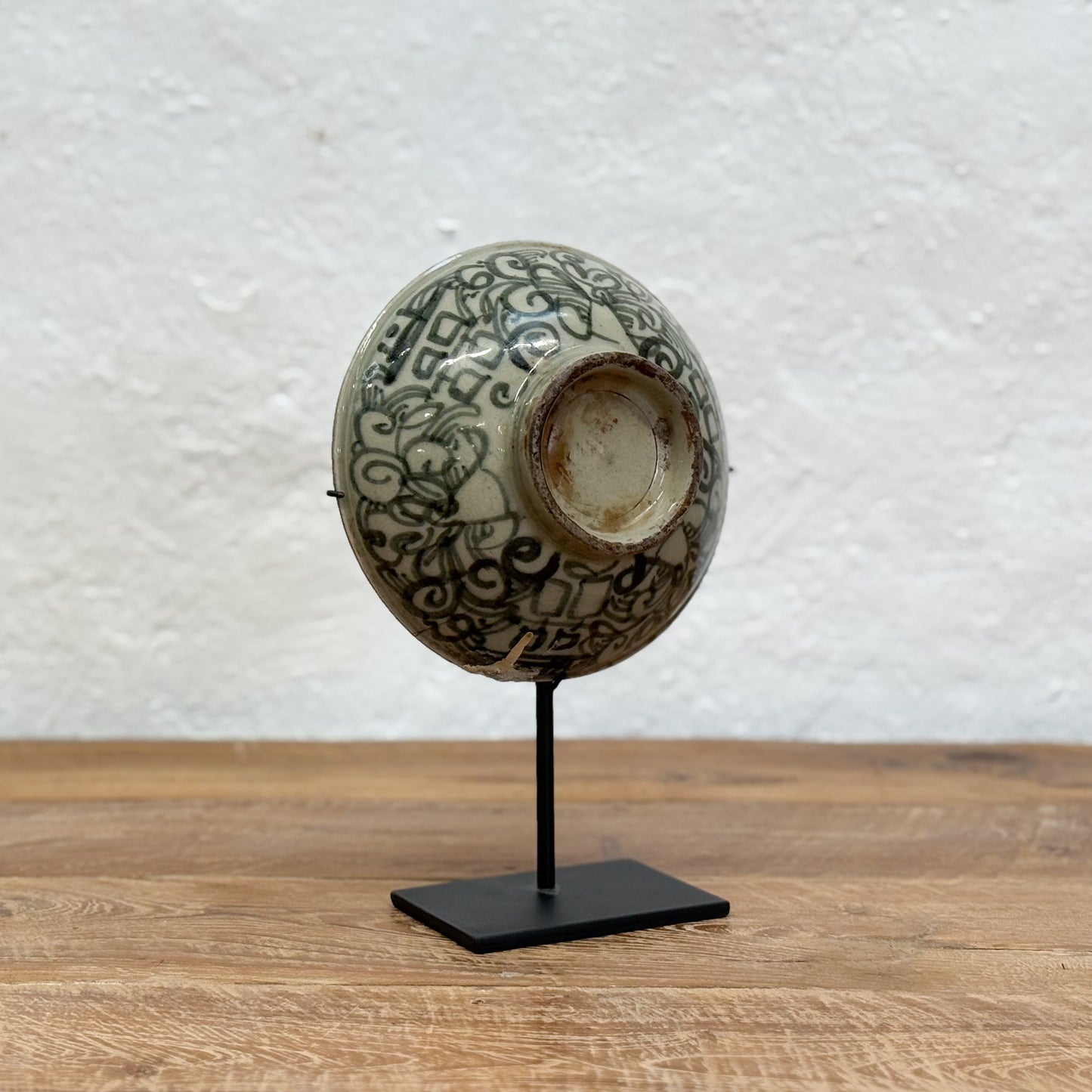 Decorative ceramic bowl with intricate patterns on a stand against a textured white wall.