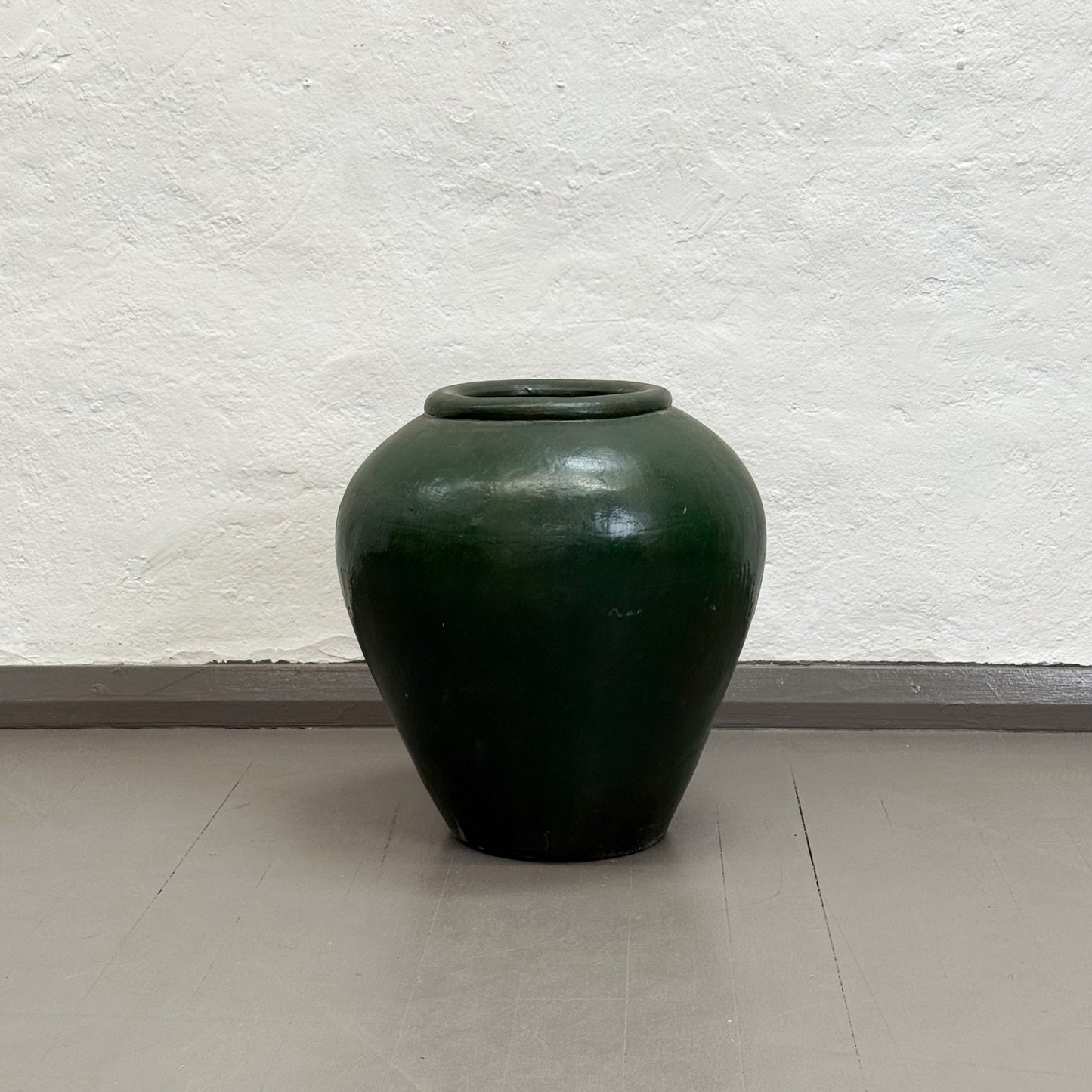 Green ceramic jar on a light gray floor with a textured white wall background